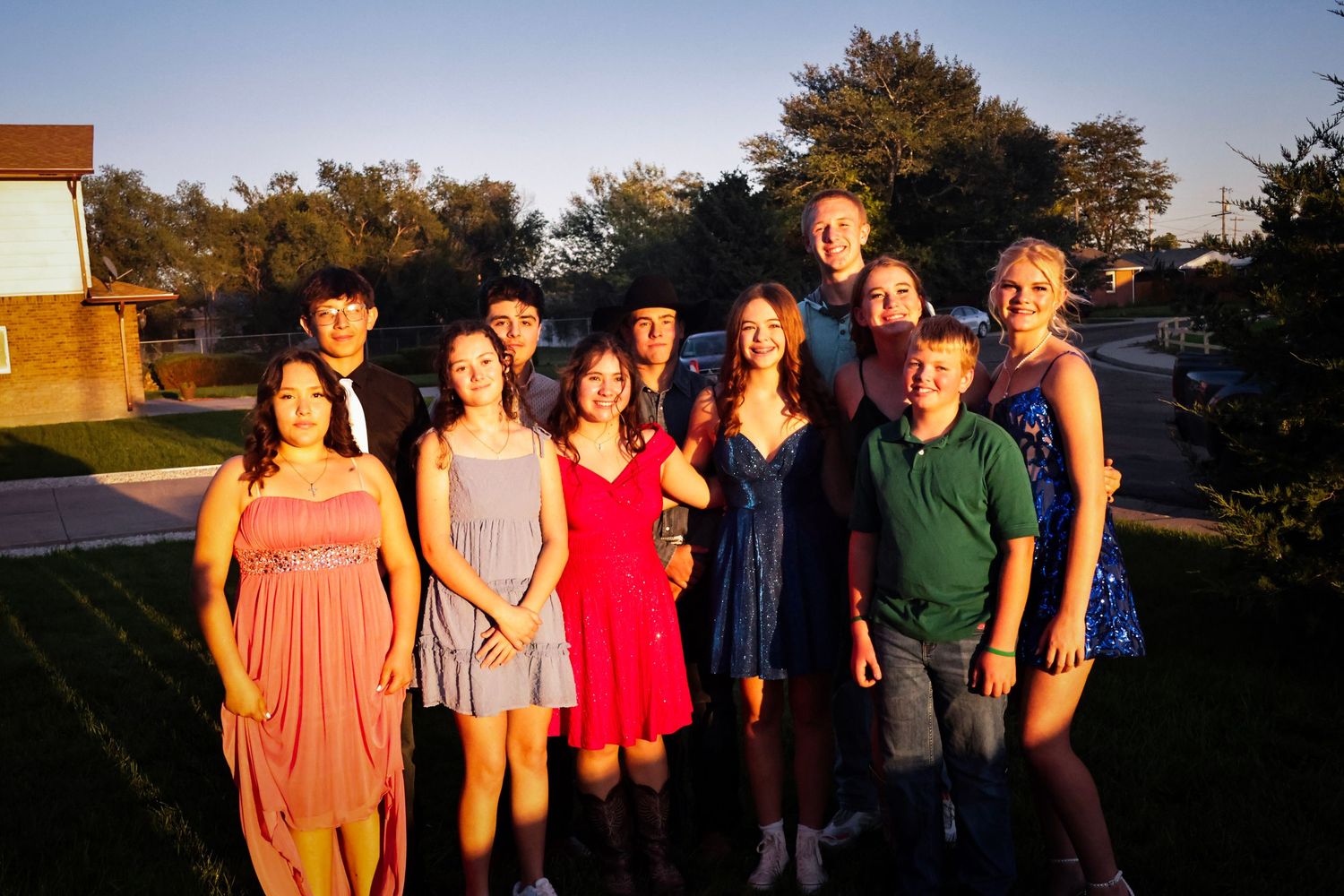 Group of eleven teenagers in semi-formal attire smiling together outdoors during a warm summer evening.