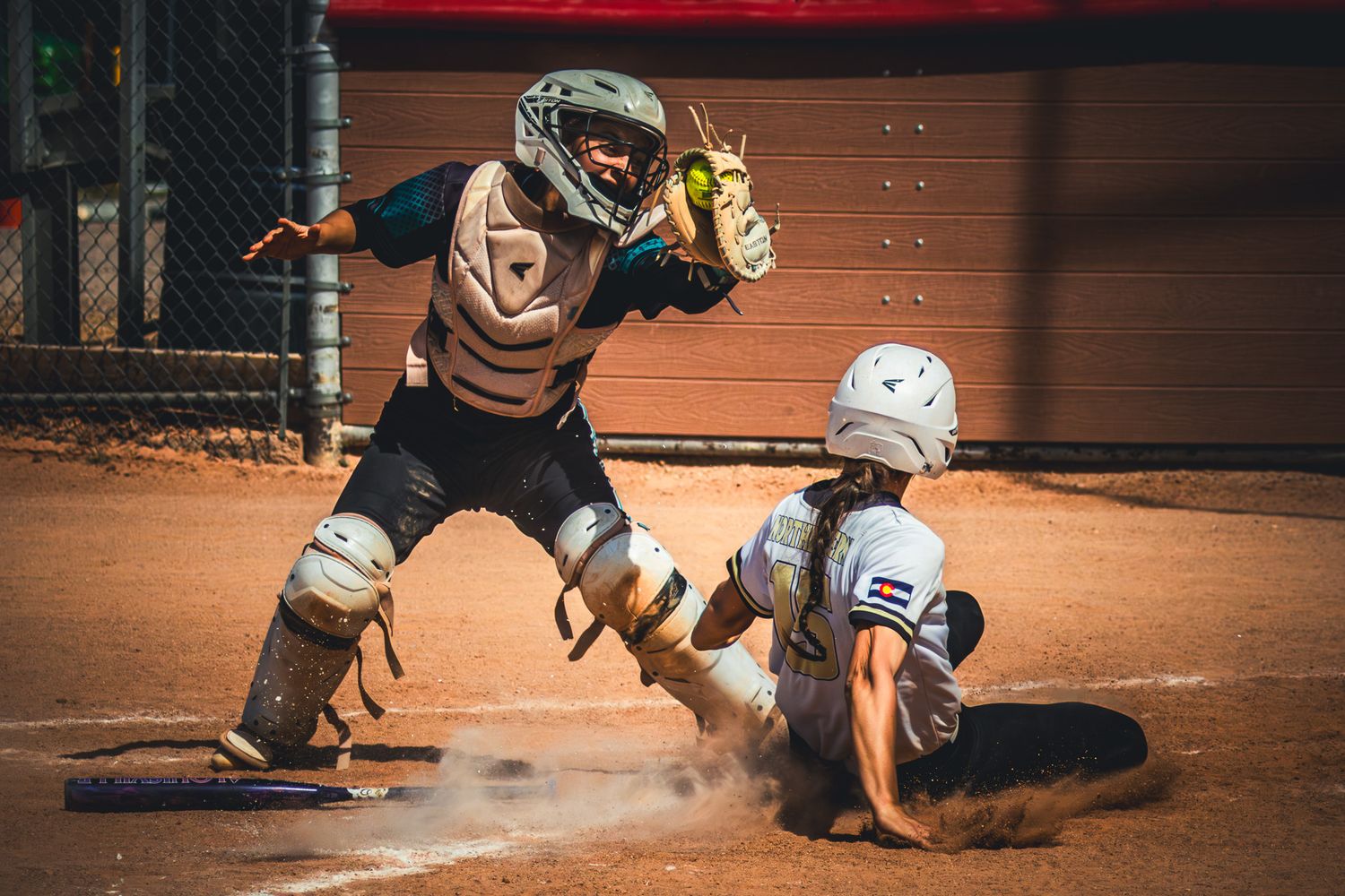 Softball catcher attempts to tag sliding runner at home plate in intense play.