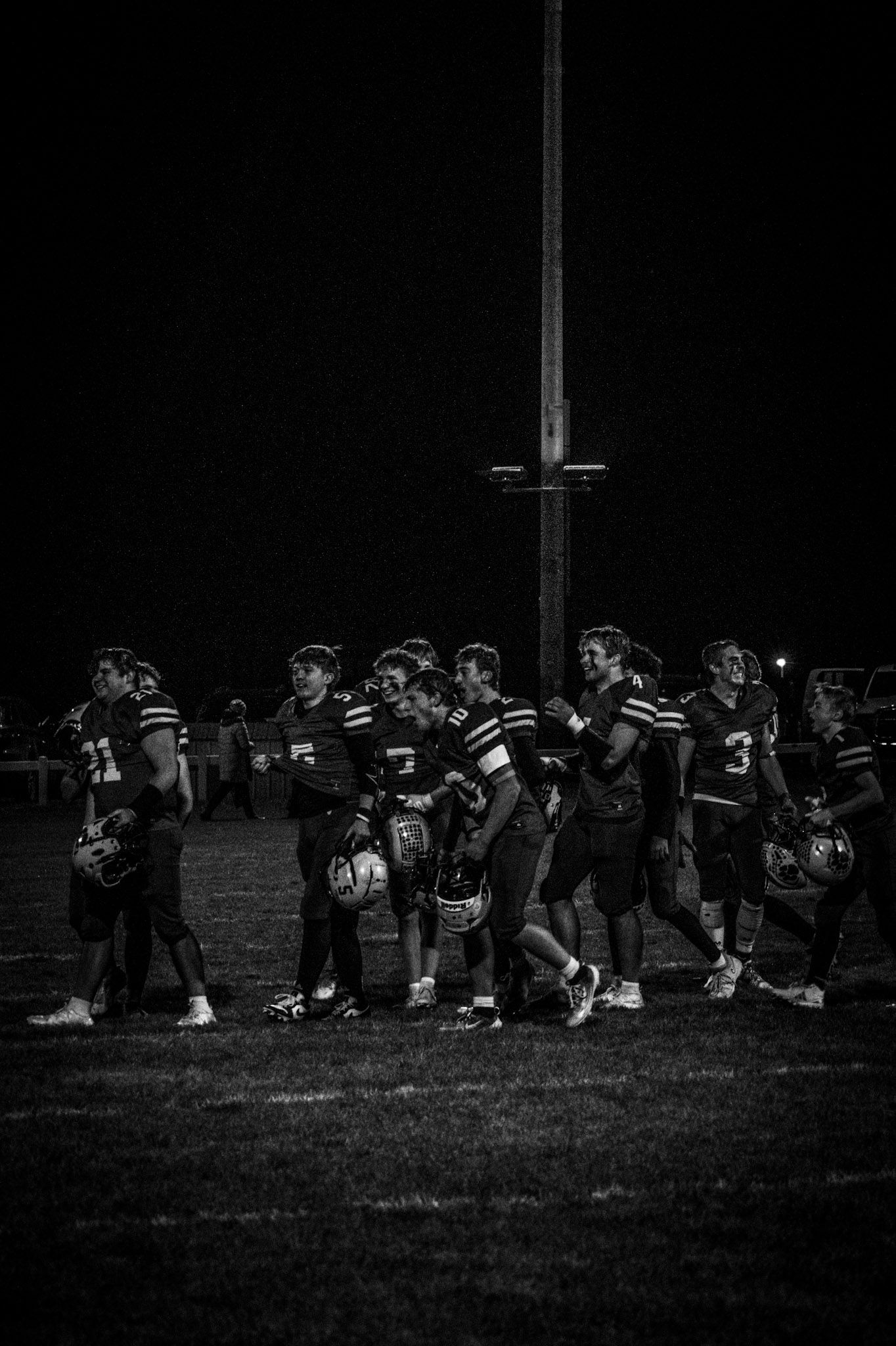 A black and white photo of a high school football team gathered together on the field at night.