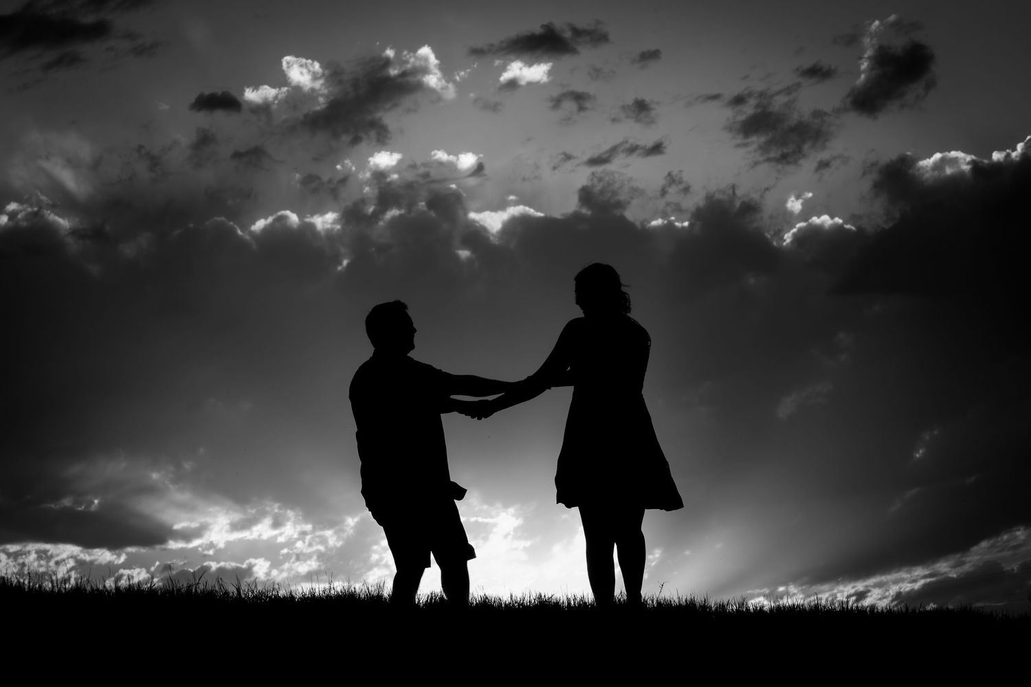 Silhouette of a romantic couple holding hands against a dramatic cloudy sky at sunset.