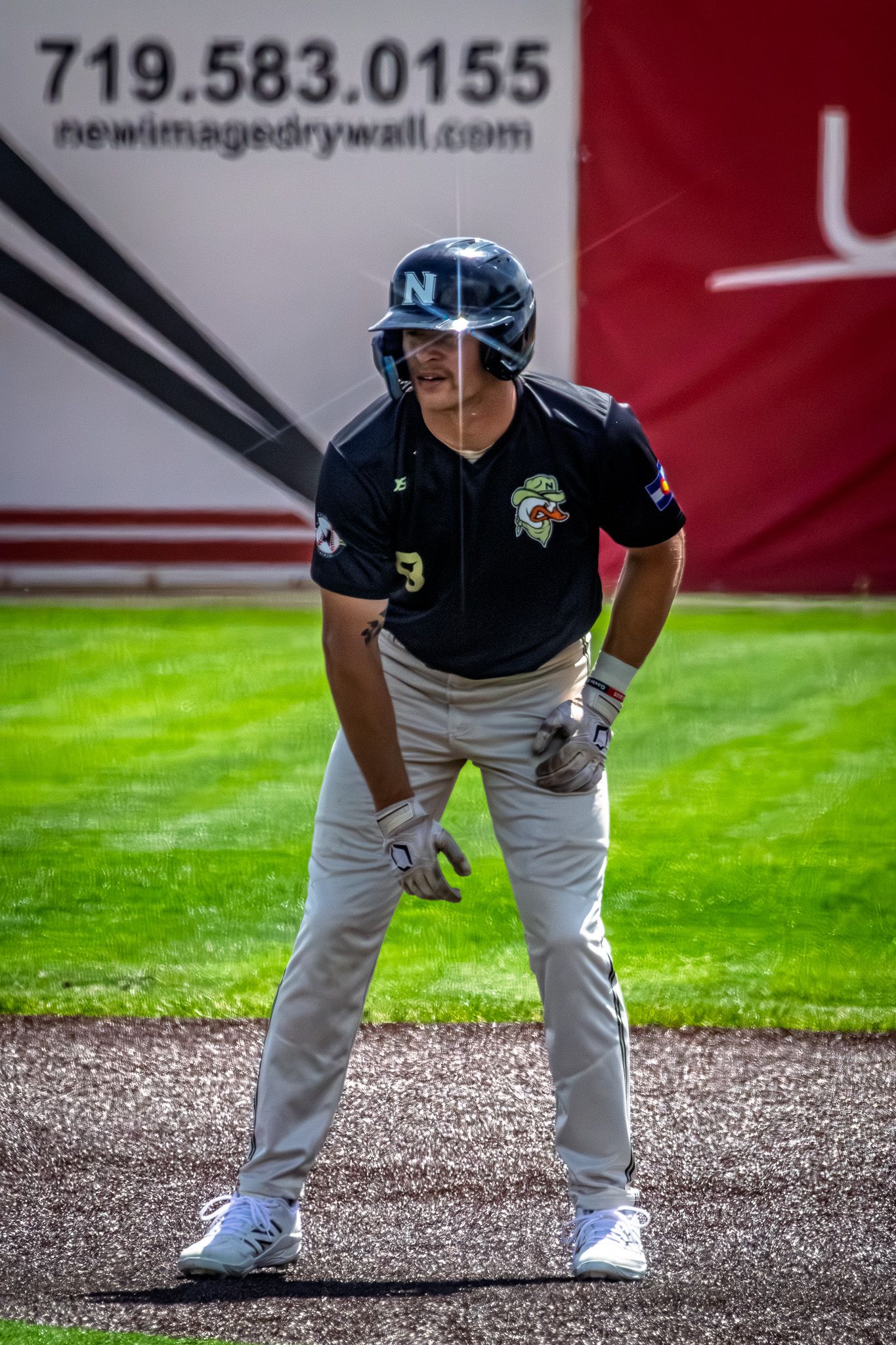 A baseball player in navy uniform stands ready on the field during a sunny game.