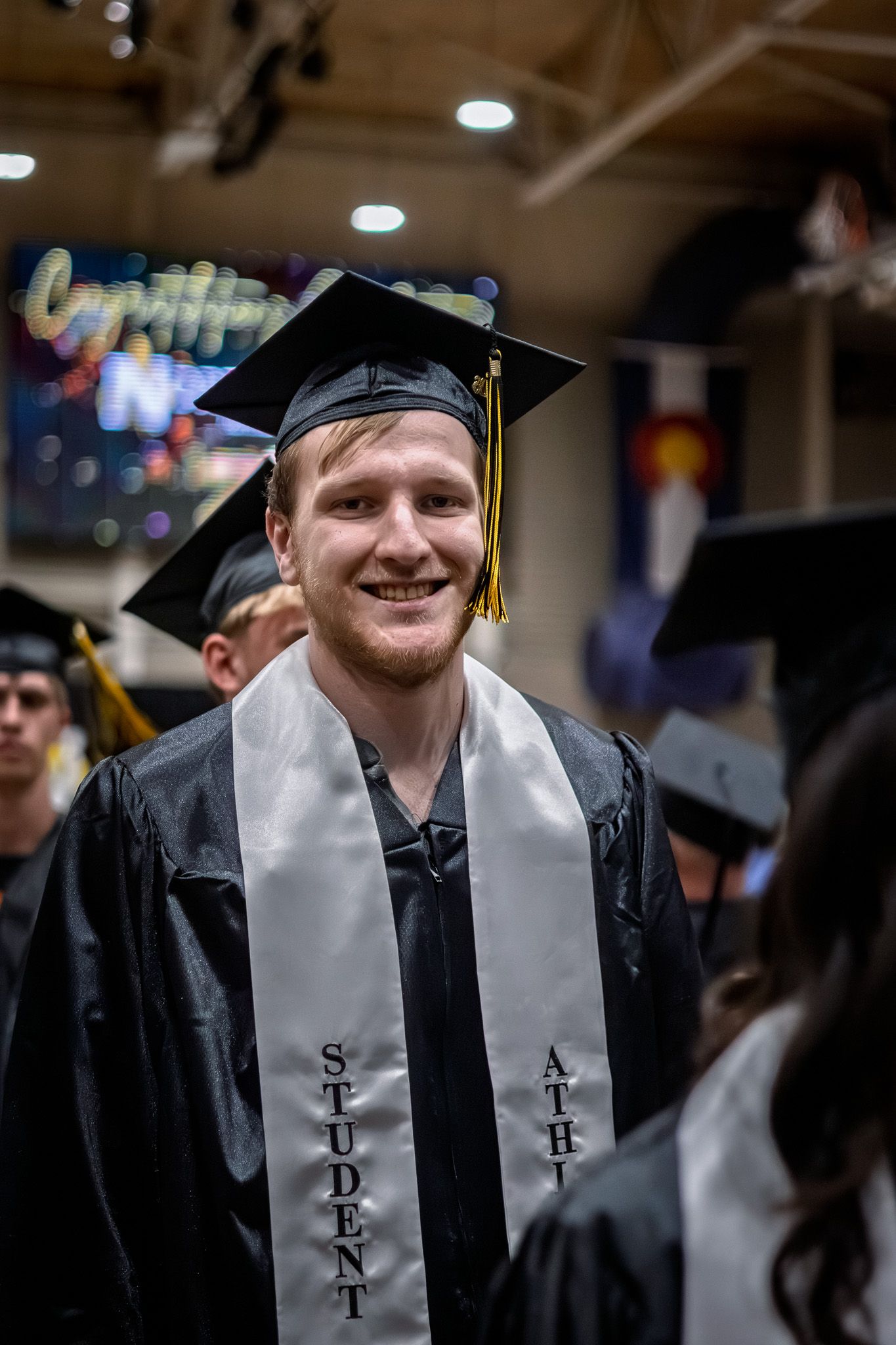 Smiling male graduate in black cap and gown with Student Athlete sash at Northeastern Junior College graduation.