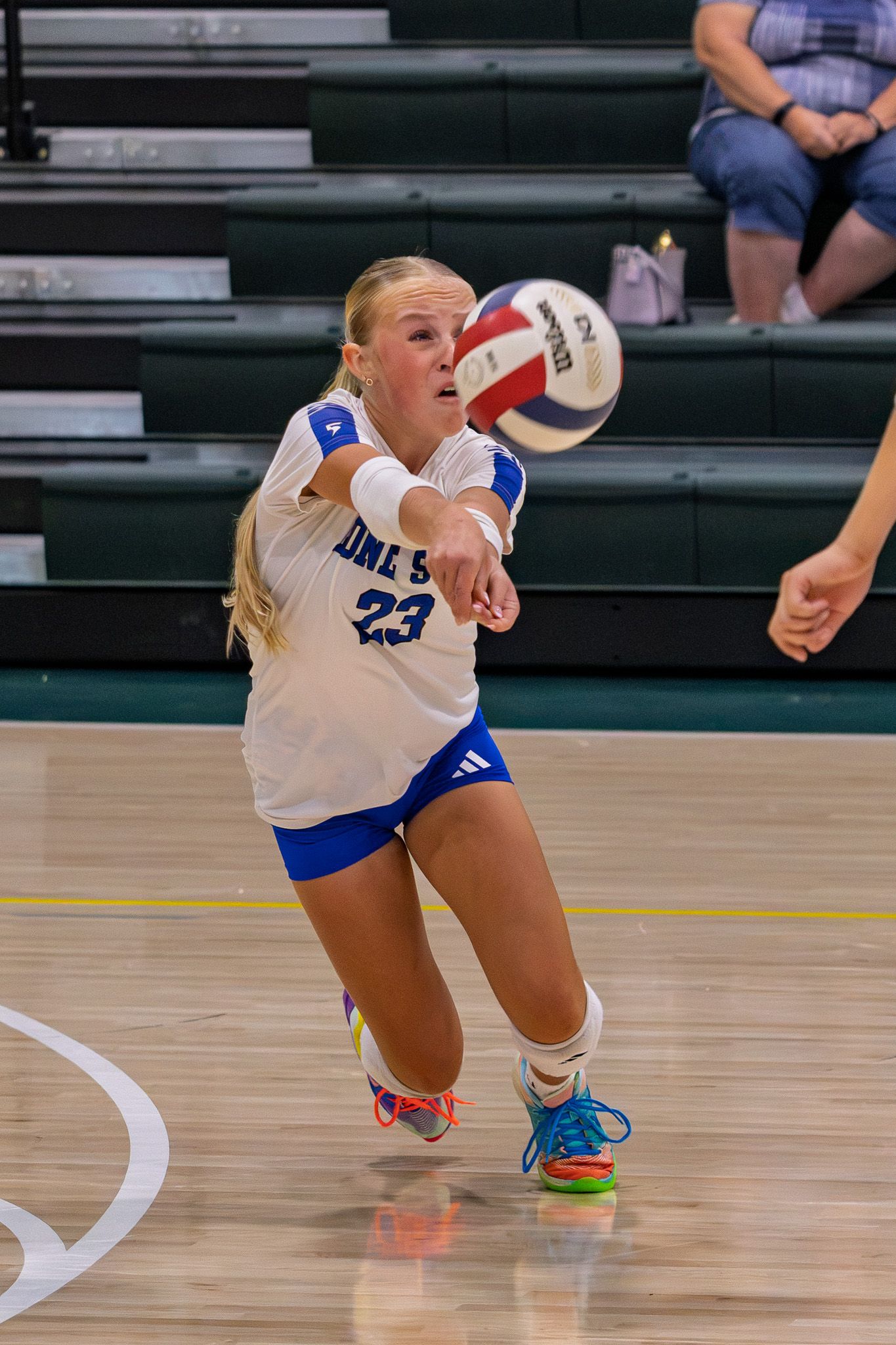 Female volleyball player #23 in blue and white uniform passes the ball during a match.