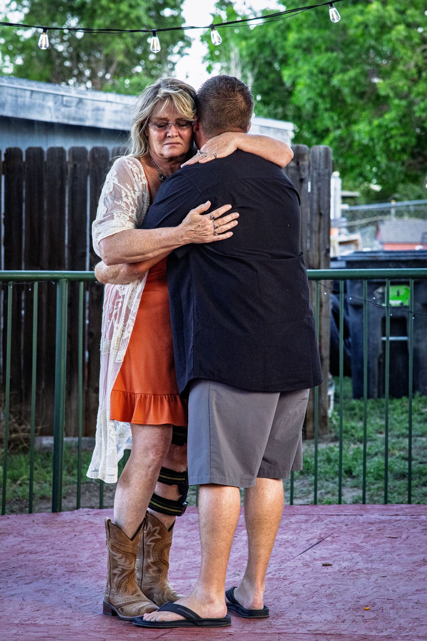 A woman in an orange dress and cowboy boots shares a warm embrace with a man at an outdoor party.