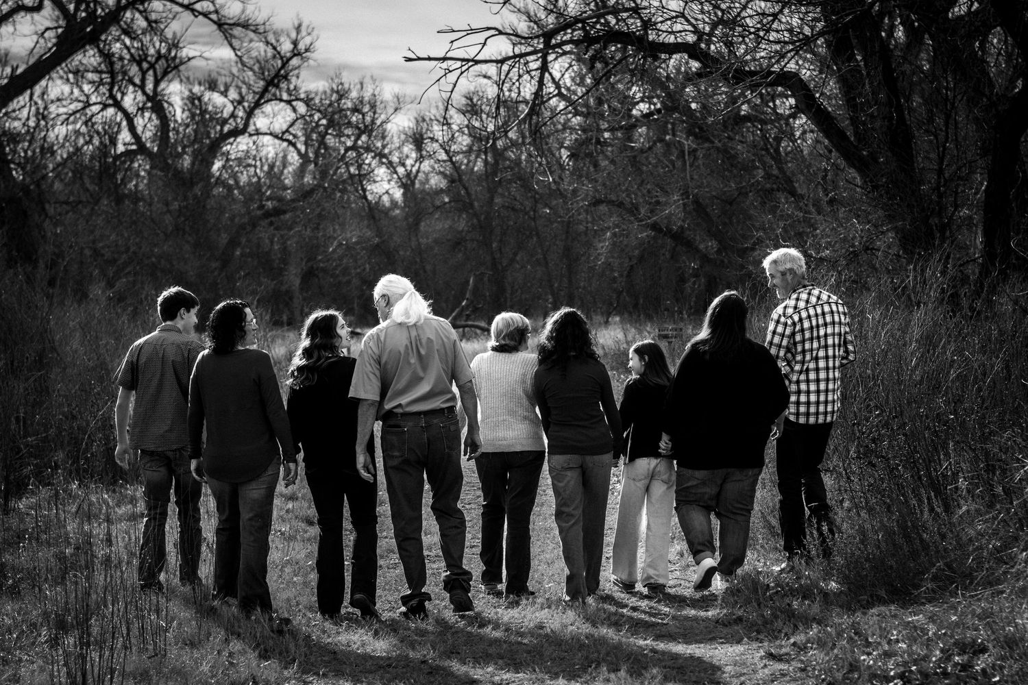 Black and white photo of large family group walking together down a rural wooded path.