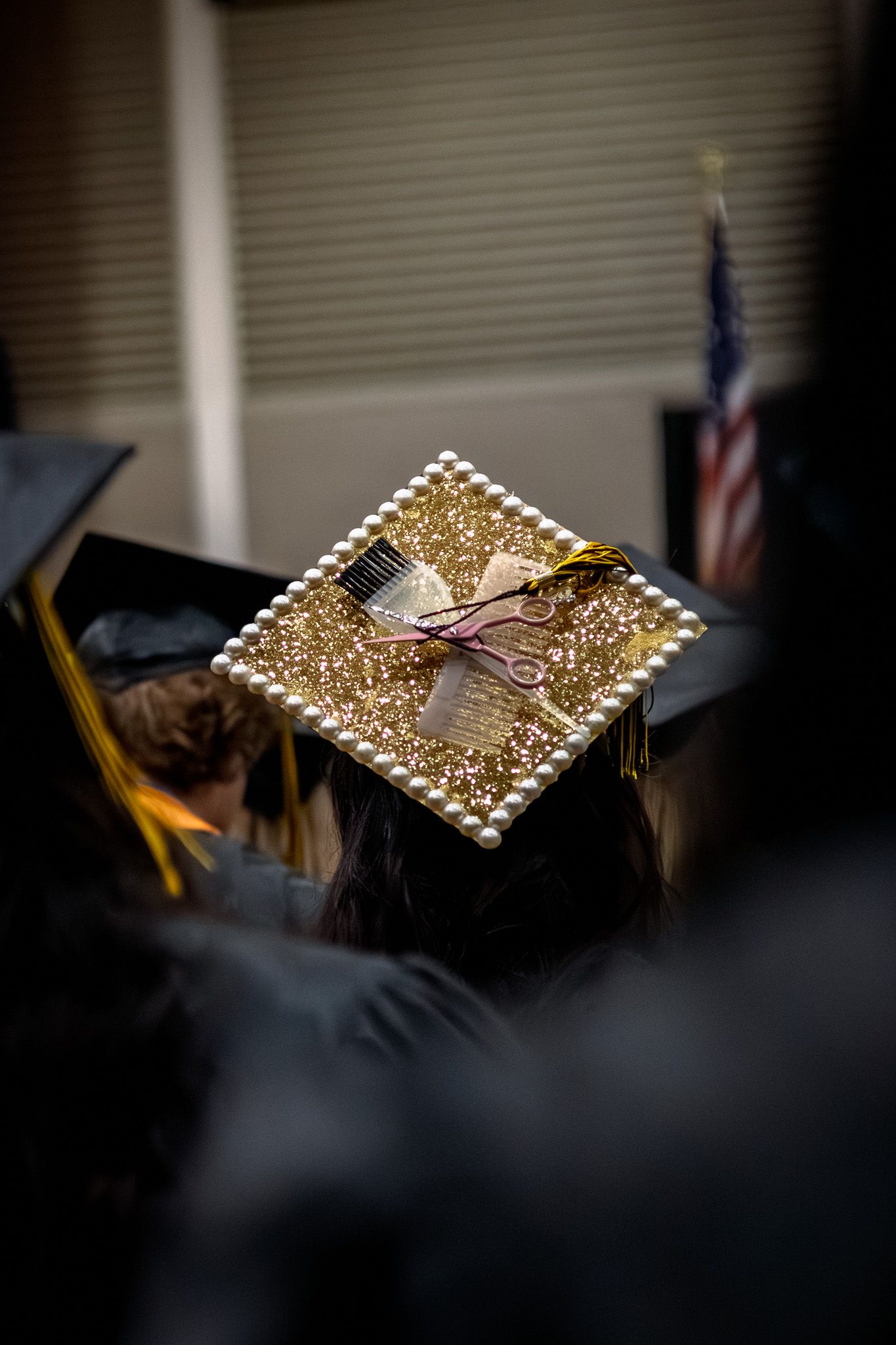 Decorated graduation cap adorned with gold glitter, pearls, scissors and comb for cosmetology graduate at commencement.