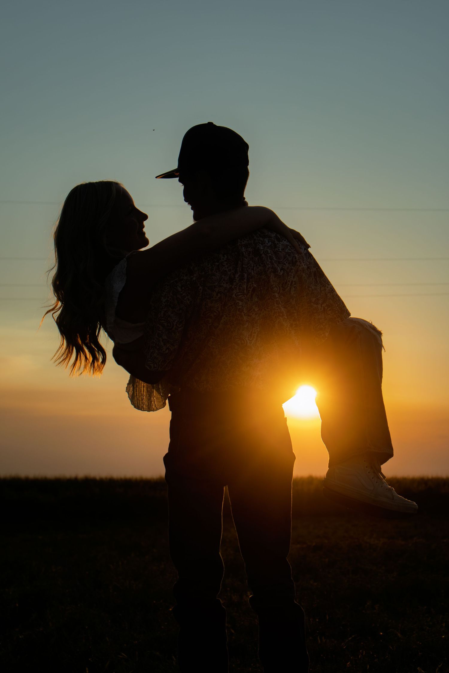 Romantic silhouette of couple, man carrying woman in arms against a vibrant golden sunset sky.