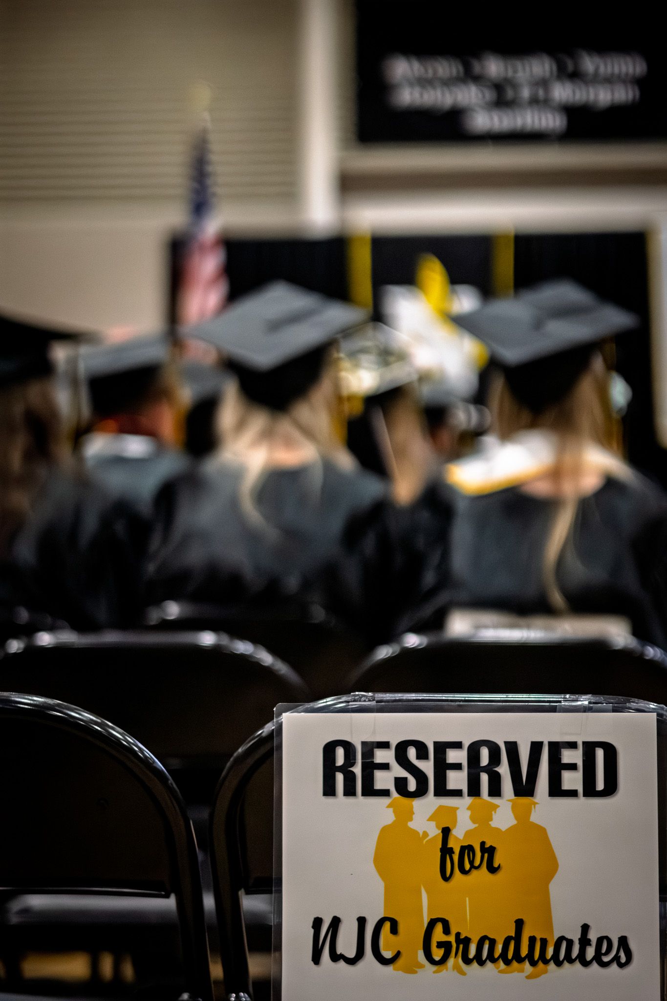 Reserved for NJC Graduates sign in front of rows of students in graduation caps and gowns.