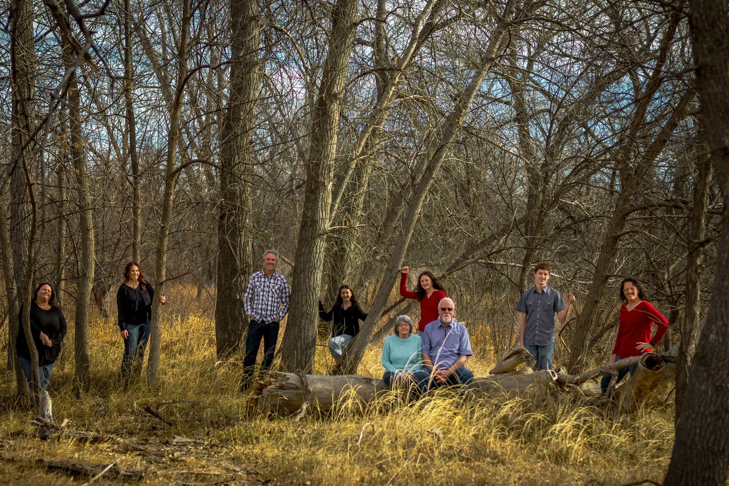 Large family group portrait among bare trees in a natural woodland setting during autumn.