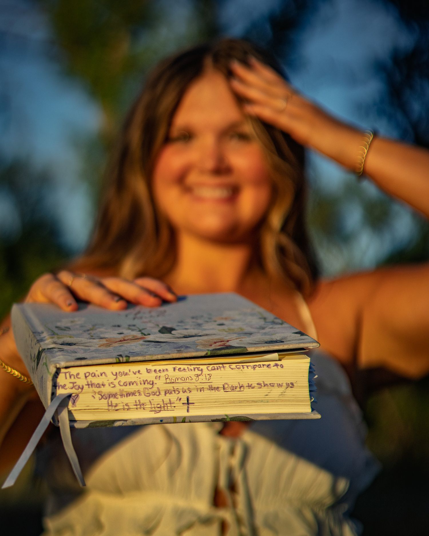 Smiling young woman holding journal with inspirational quote in warm golden outdoor lighting.