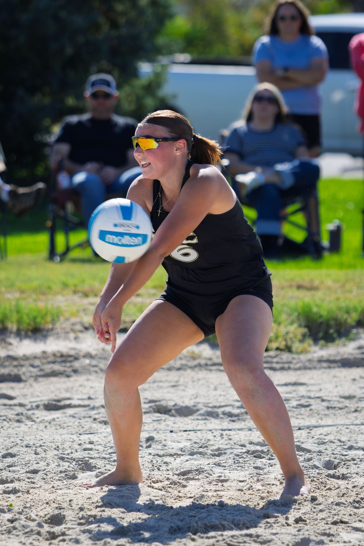 Female beach volleyball player in black uniform preparing to bump a Molten volleyball during a sunny outdoor game.