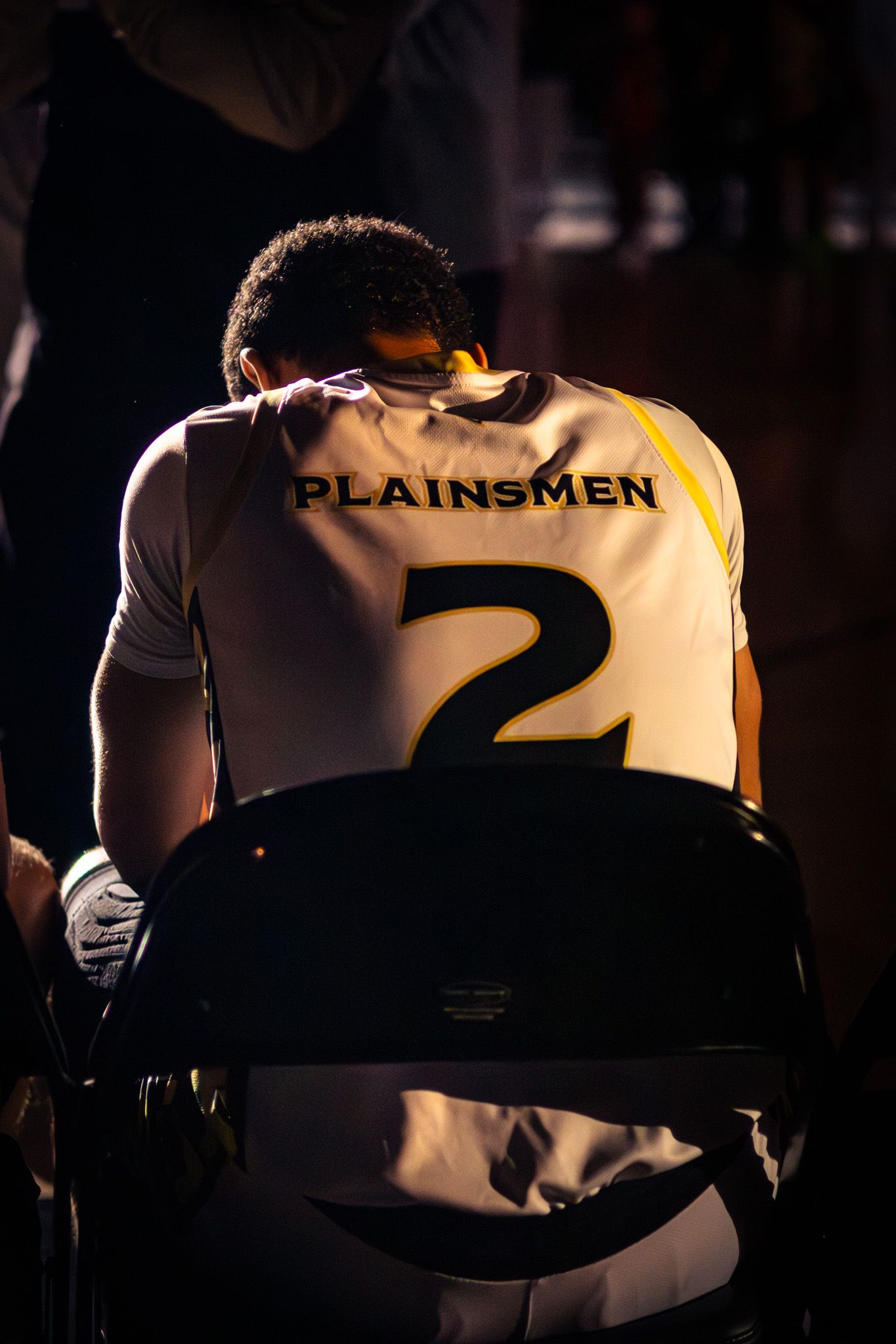 Plainsmen player #2 sits with head bowed in a white and gold jersey before a basketball game.