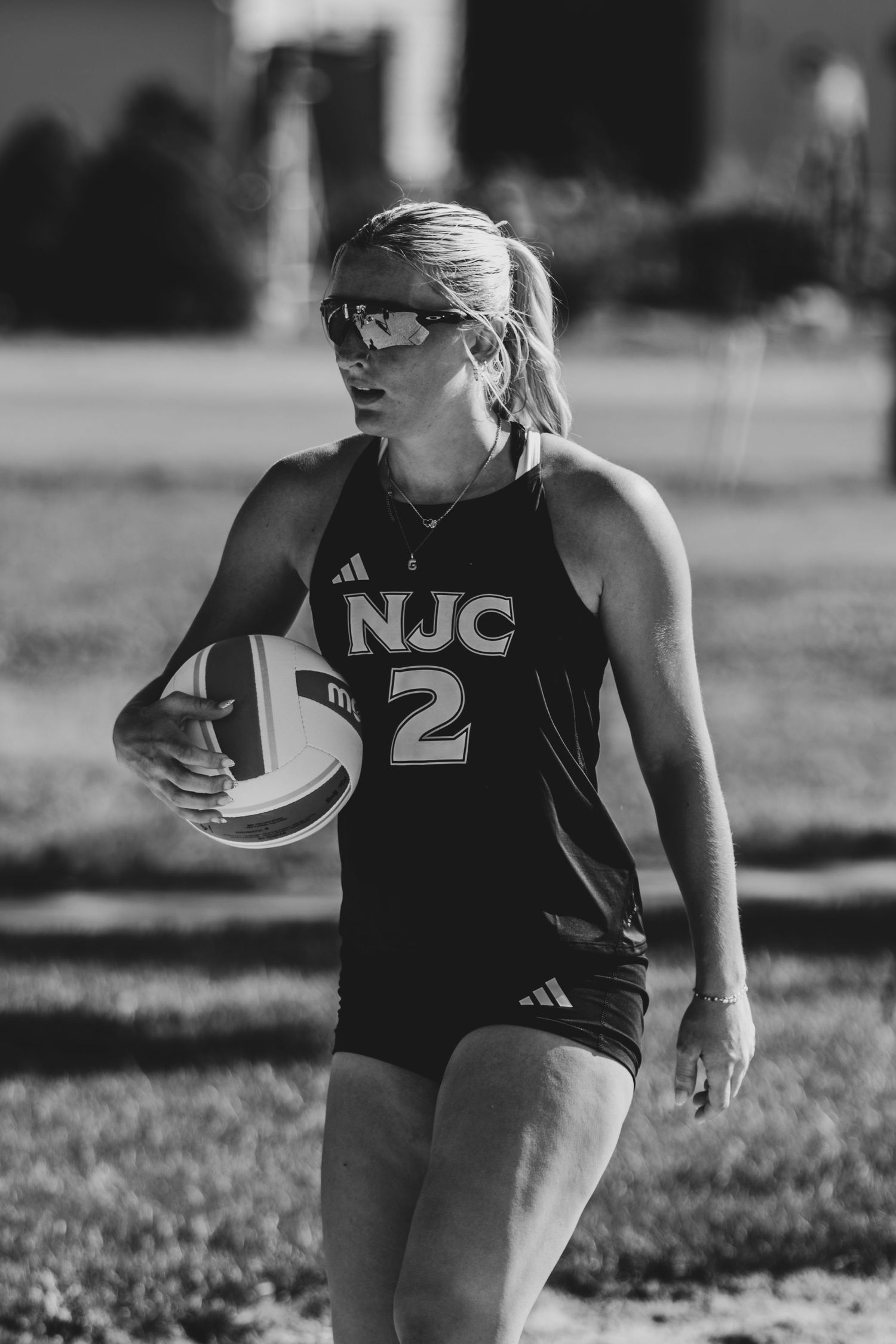 Black and white photo of female NJC number 2 volleyball player holding a ball on outdoor court.