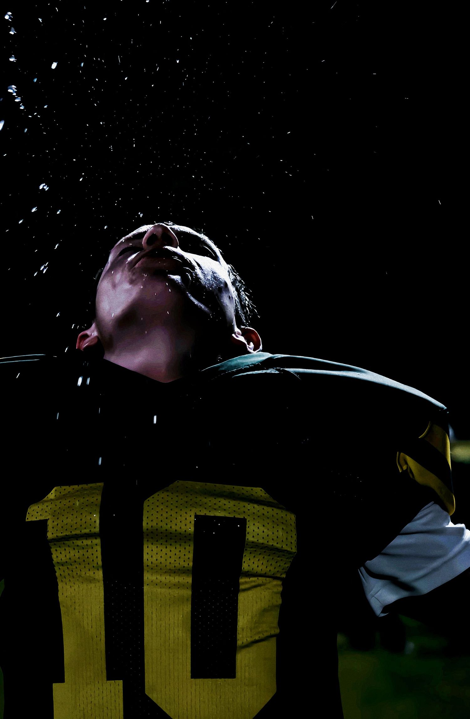 Close-up dramatic shot of football player #10 with water droplets splashing in dark light.