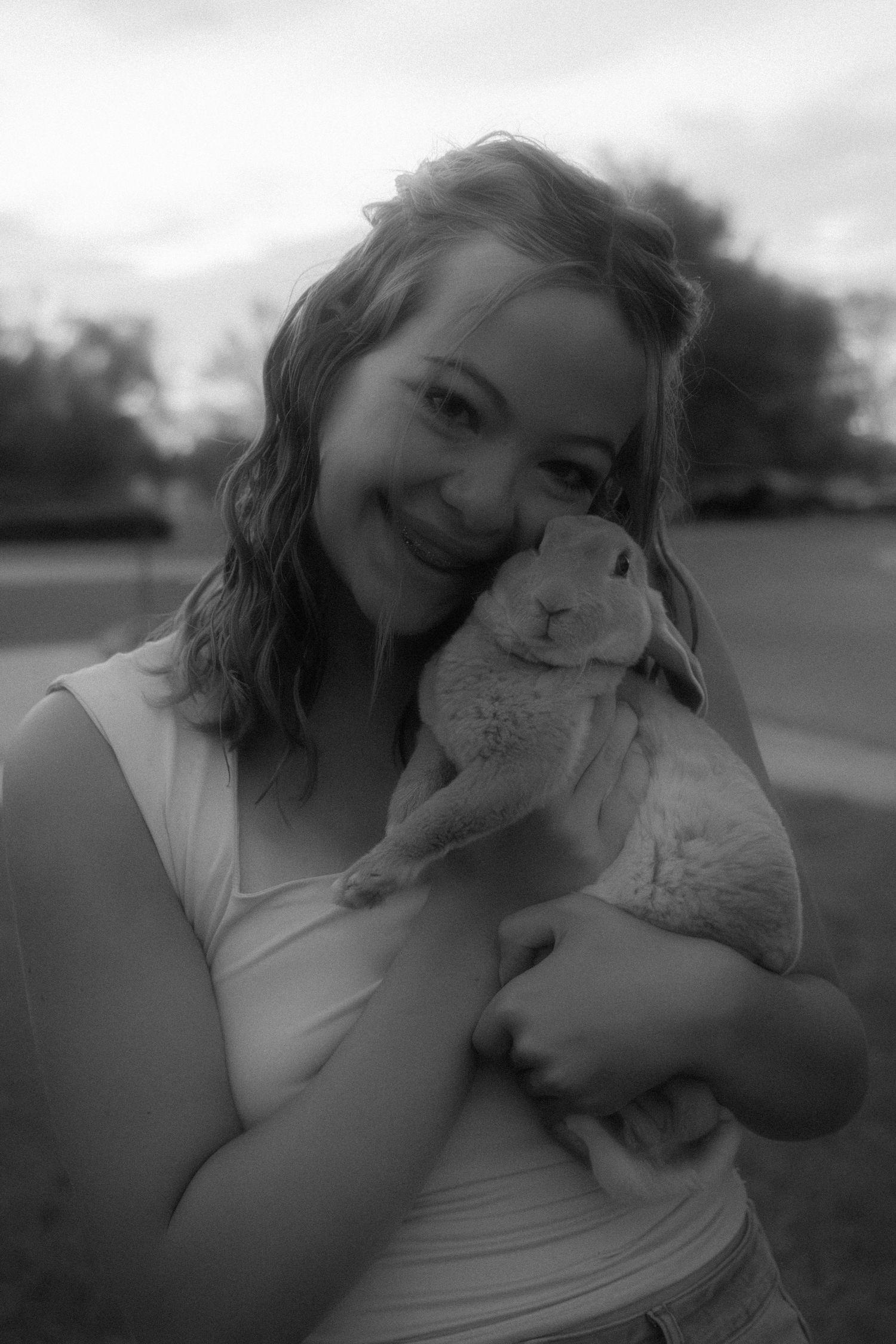 Black and white photo of a smiling woman cuddling a rabbit outdoors.