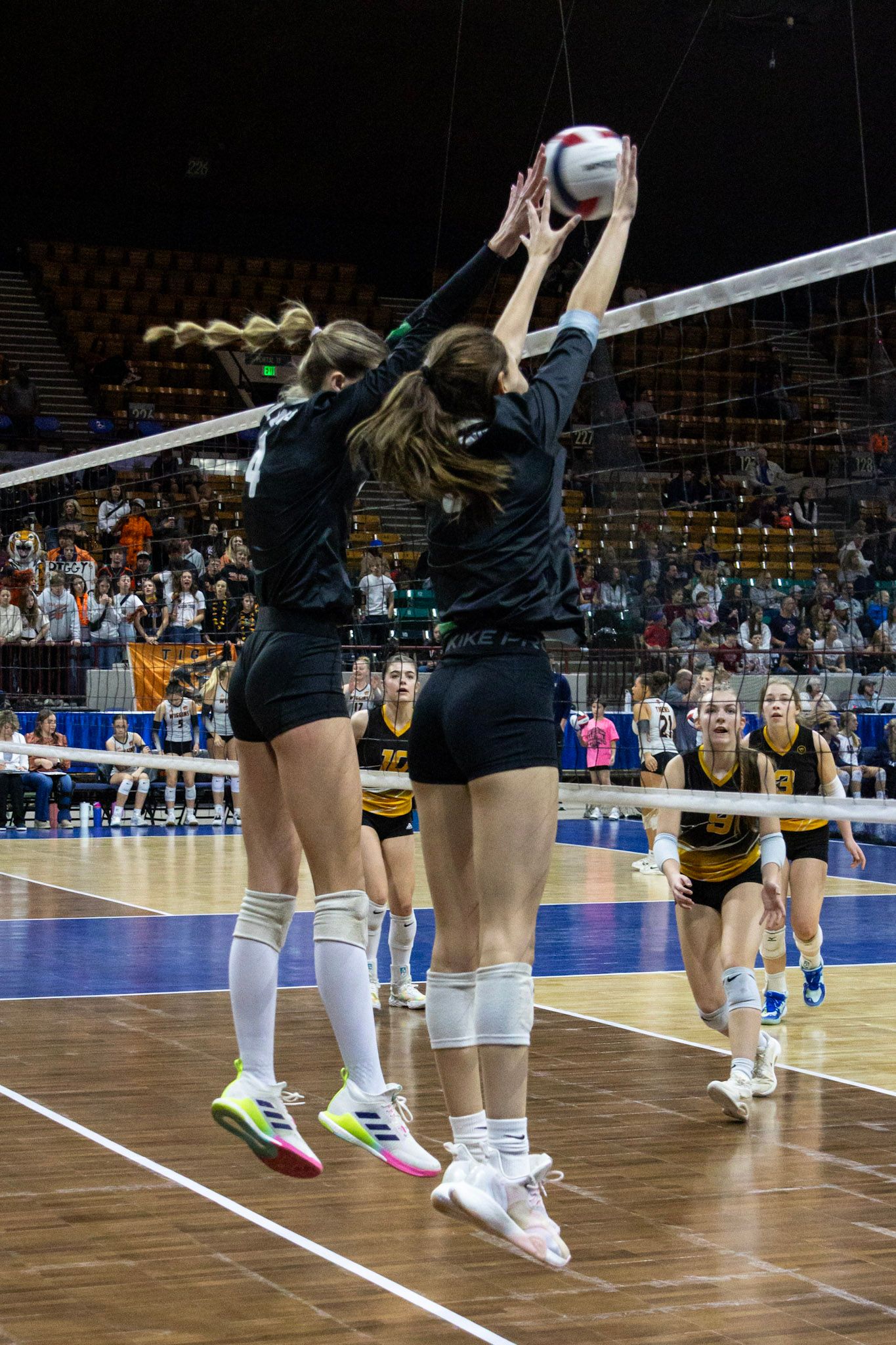 Two volleyball players block at the net during competitive indoor tournament match.