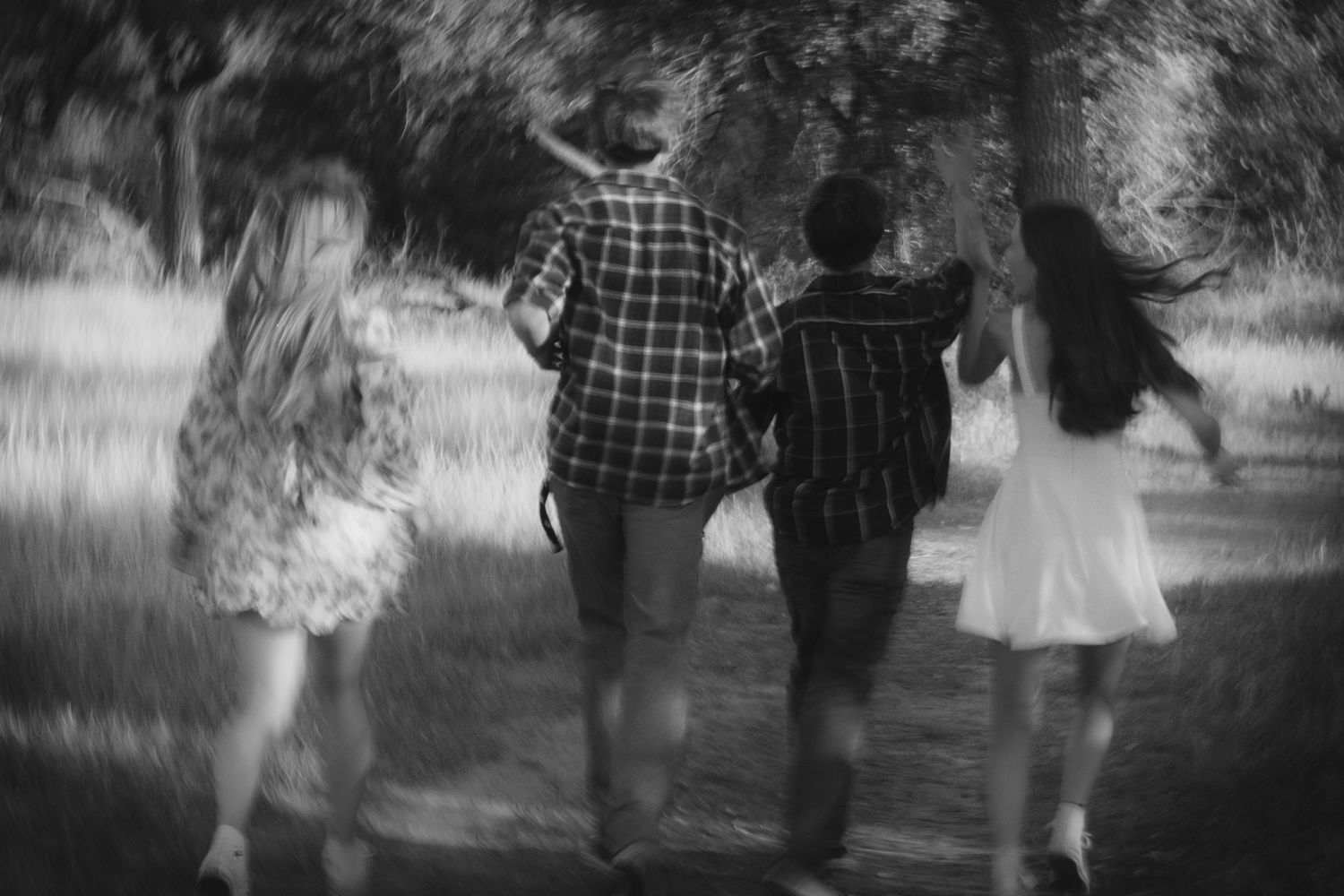 Black and white photo of three friends walking together down a tree-lined path in a park.