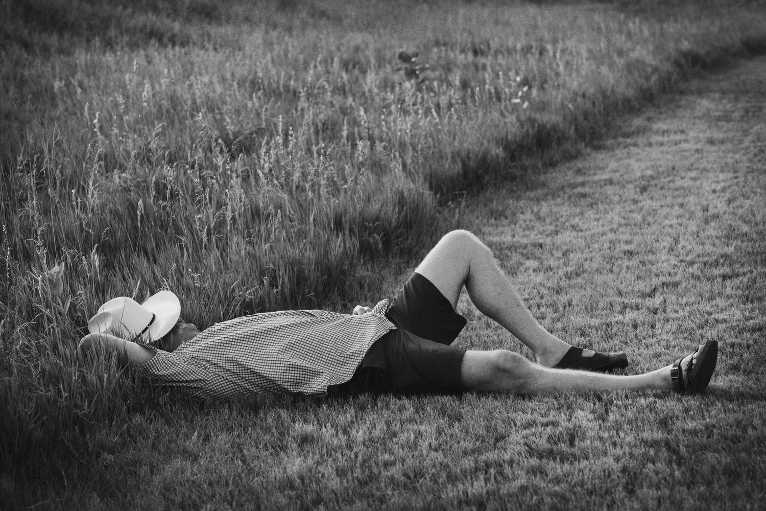 Black and white photo of couple lying together in a grassy field pathway.