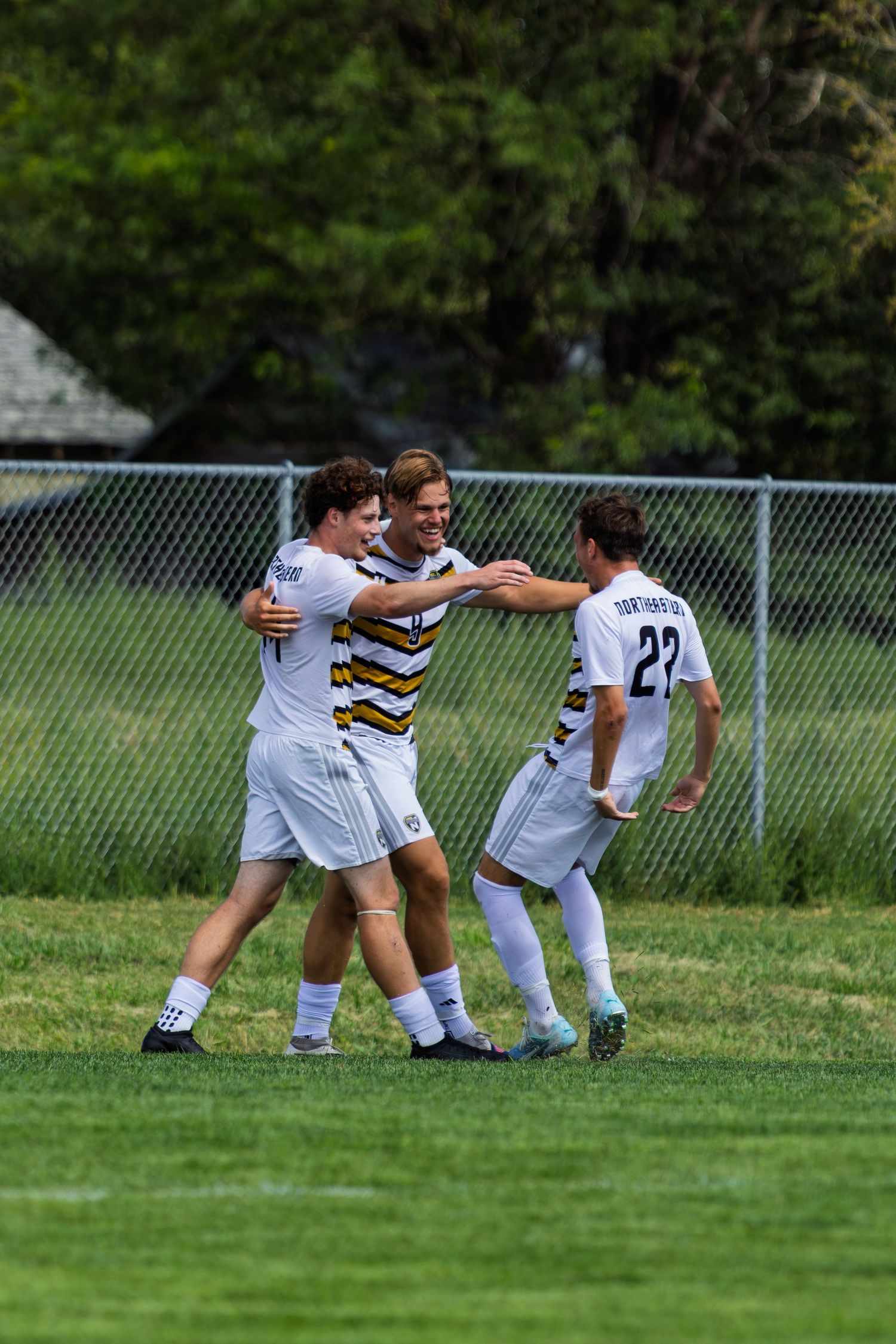 Three Northwestern soccer players celebrate together on the field after scoring a goal.