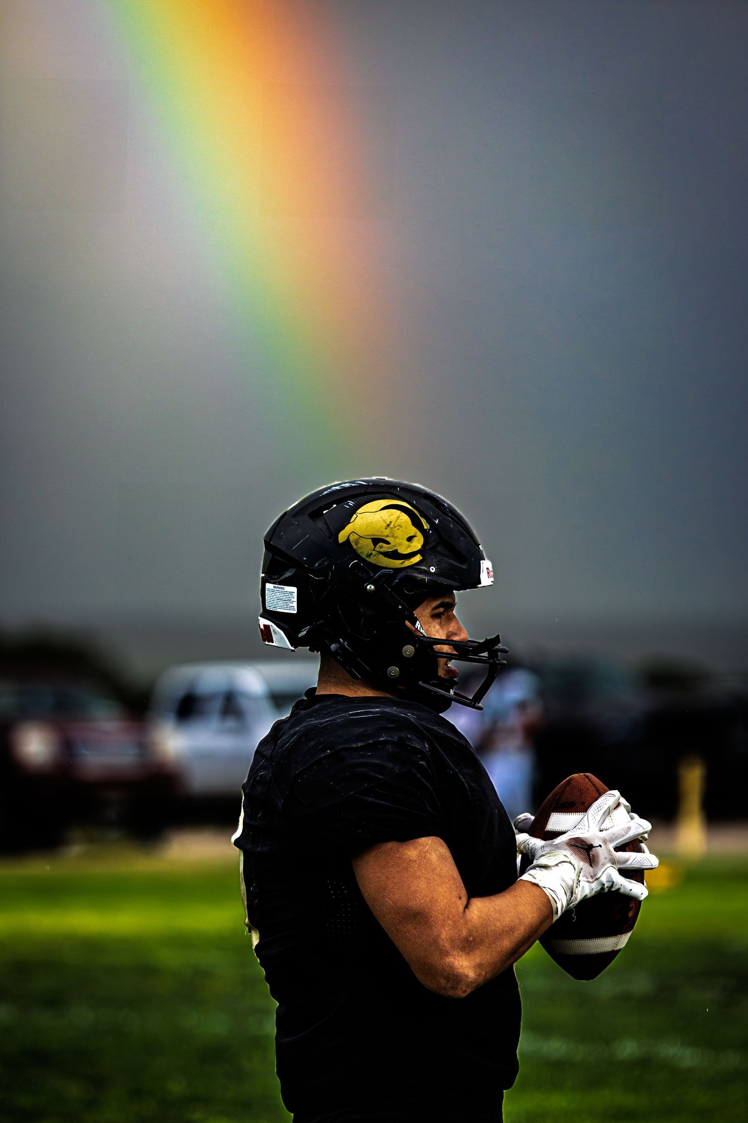A football player holds a ball while a vibrant rainbow arcs through the stormy sky behind him.
