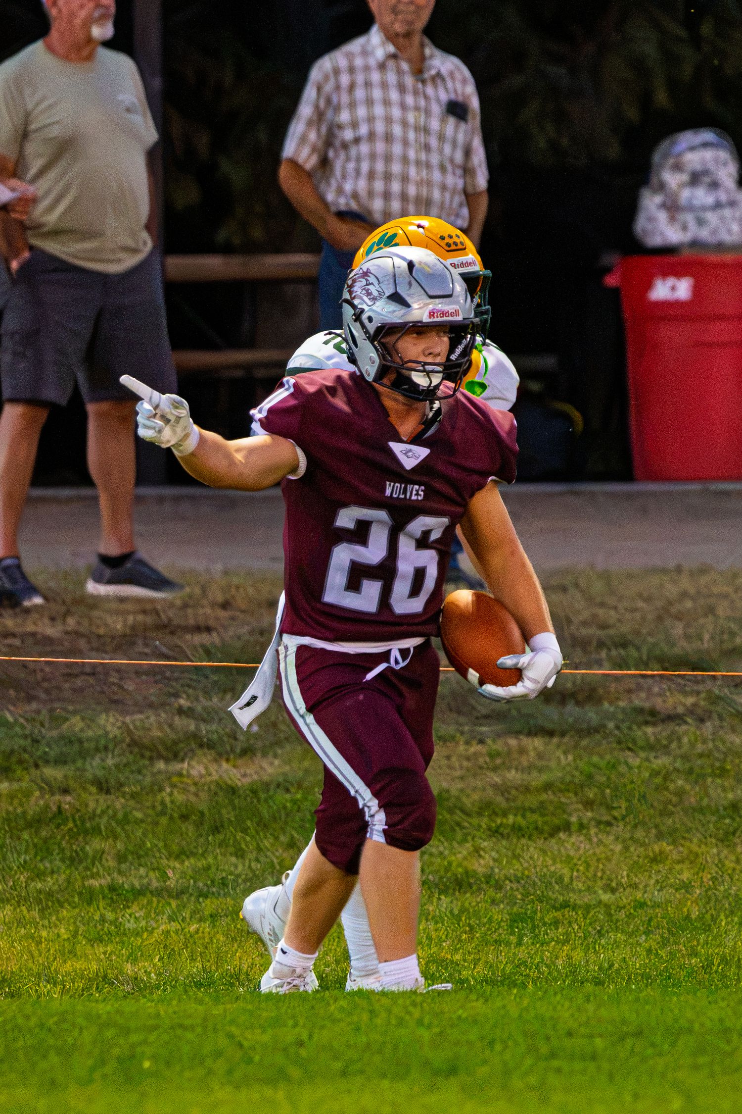 Youth football player #26 in maroon Wolves uniform points downfield while carrying the ball during a game.