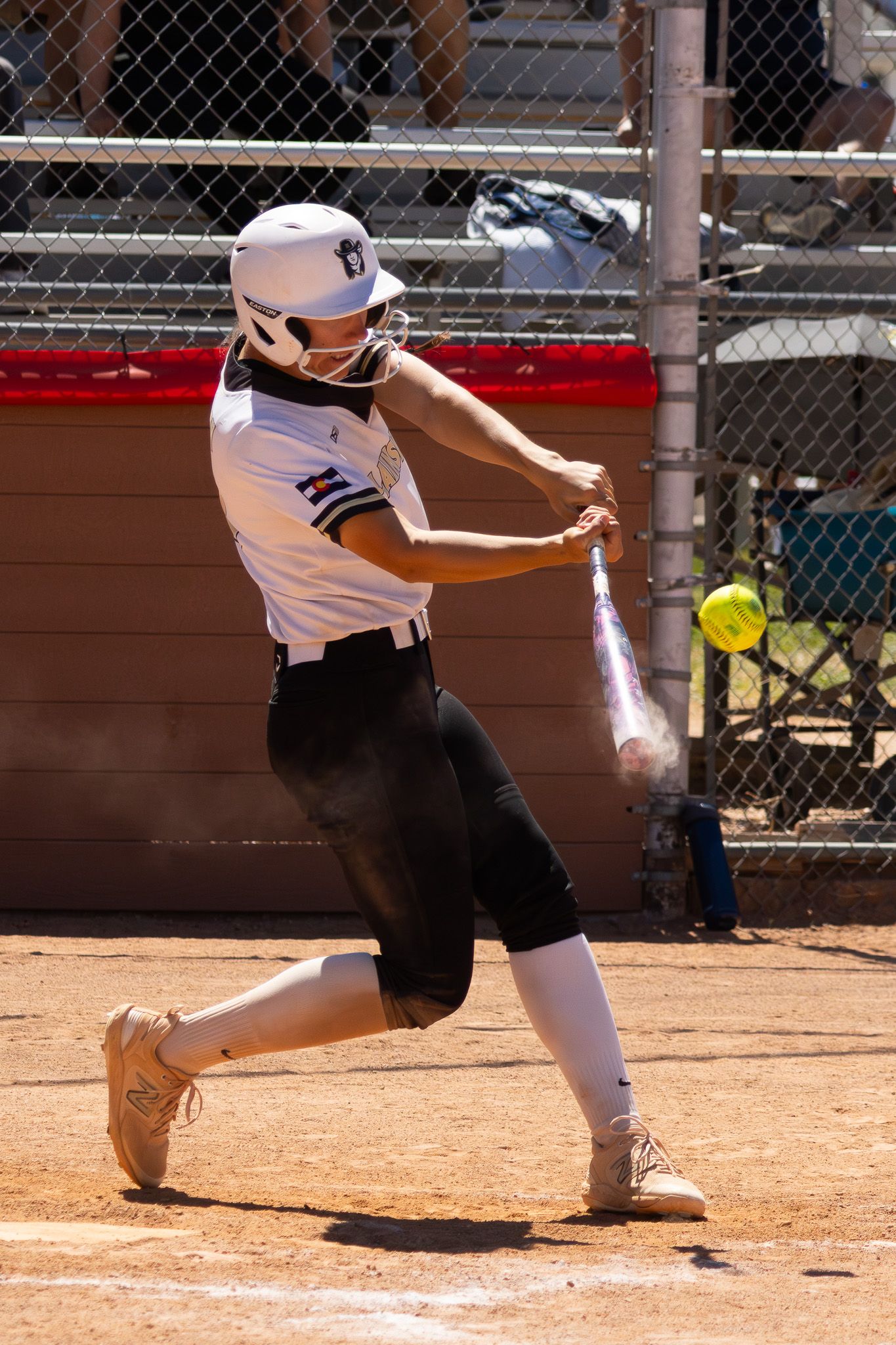 Female softball batter makes solid contact with yellow ball during competitive game.