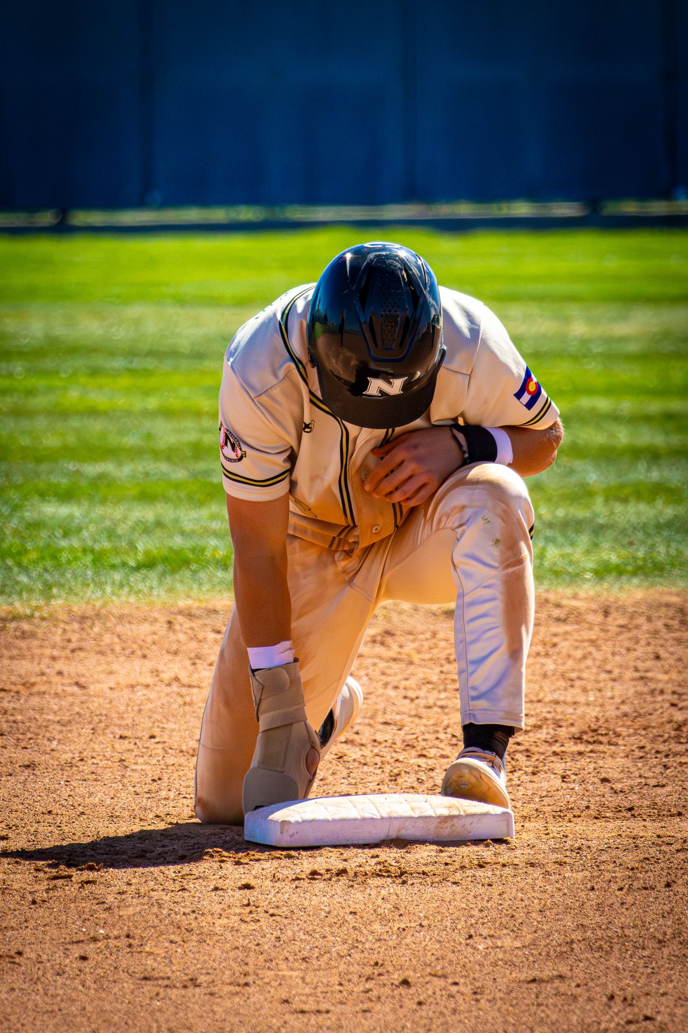 A baseball player kneels on a base with head down in a moment of disappointment or prayer.