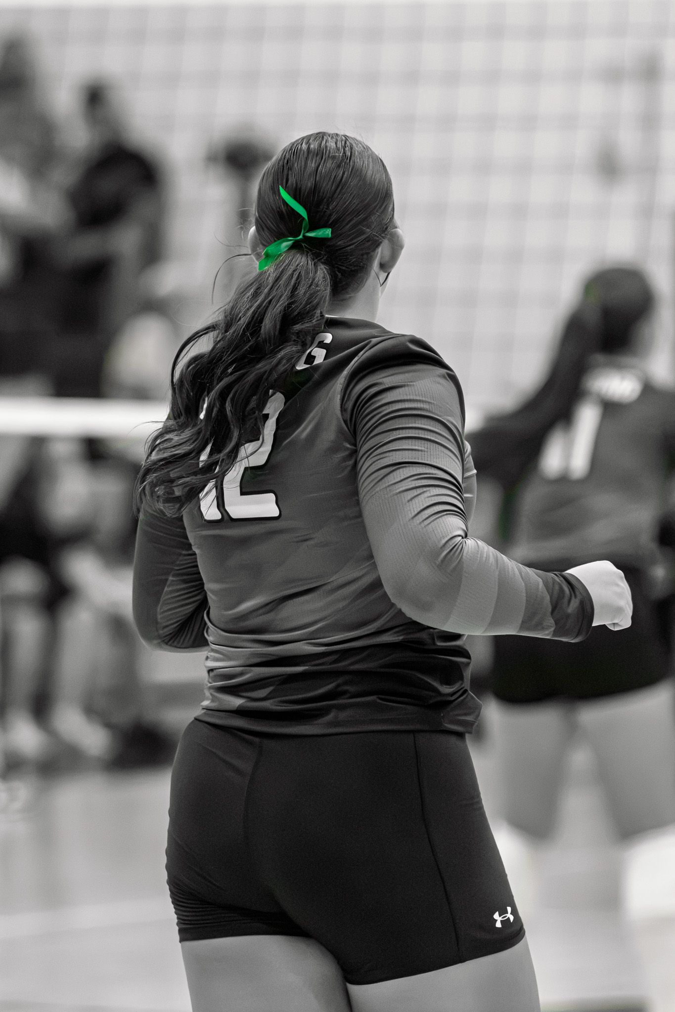 Female volleyball player #12 in black uniform with green hair tie, selective color black and white photo.