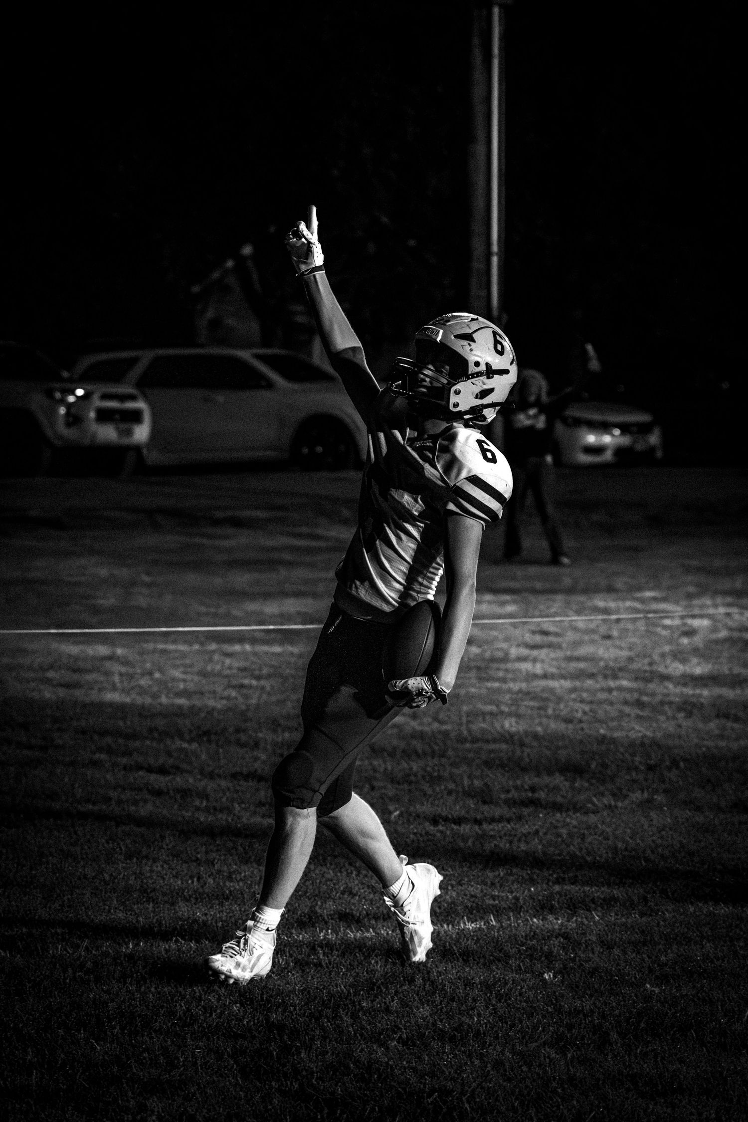 Black and white photo of a football player pointing skyward in celebration during a night game.