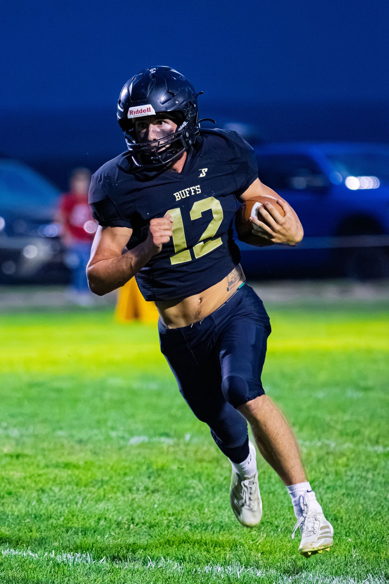Football player number 12 in black Buffs uniform running with the ball during an evening game.