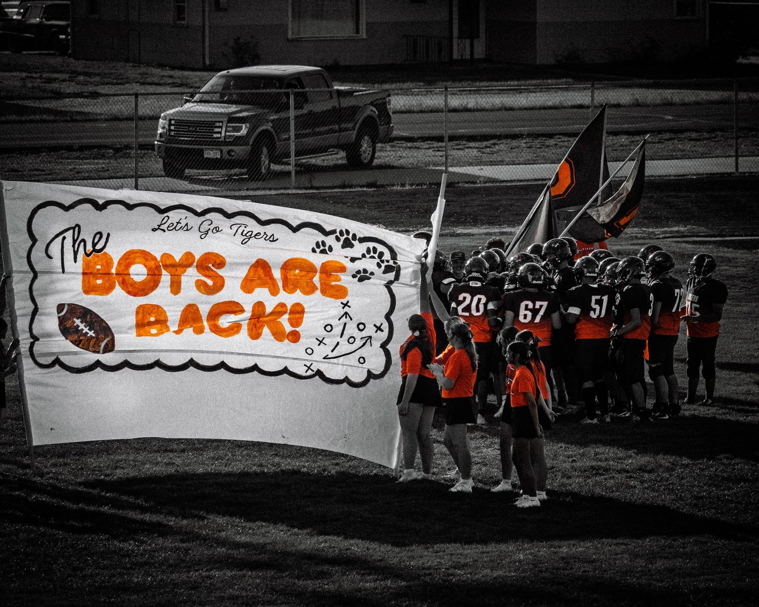 Tigers football team huddles behind a banner reading The Boys Are Back in black and white photo.