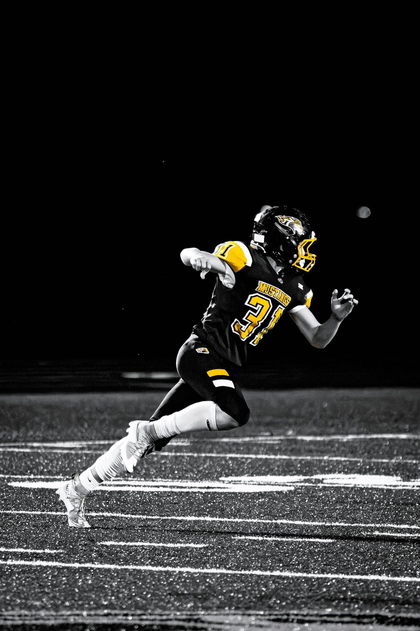 High school football player number 31 in black and gold uniform sprinting down the field during a night game.