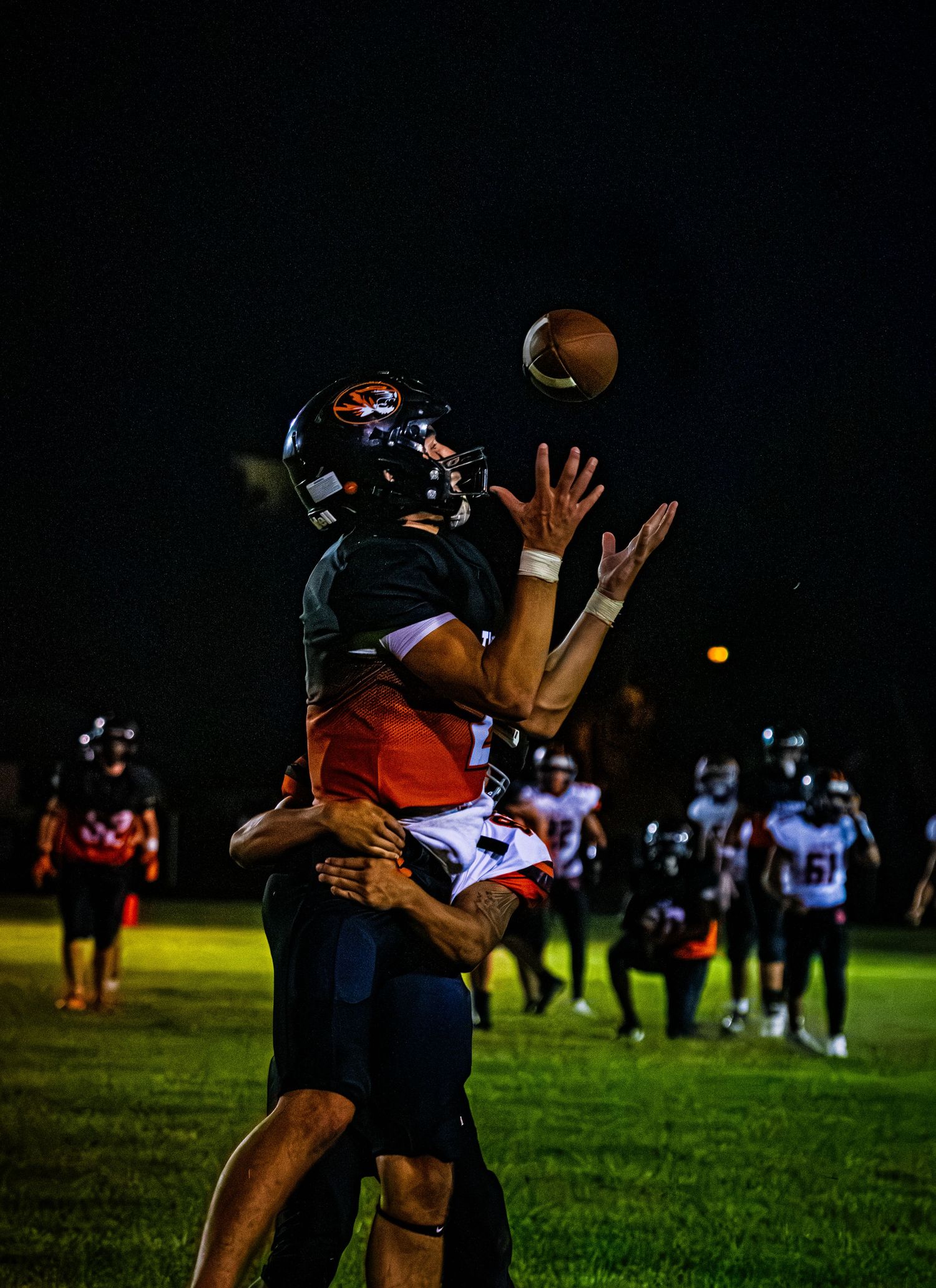 Two football players jump to catch a pass under the lights during a night game on the field.