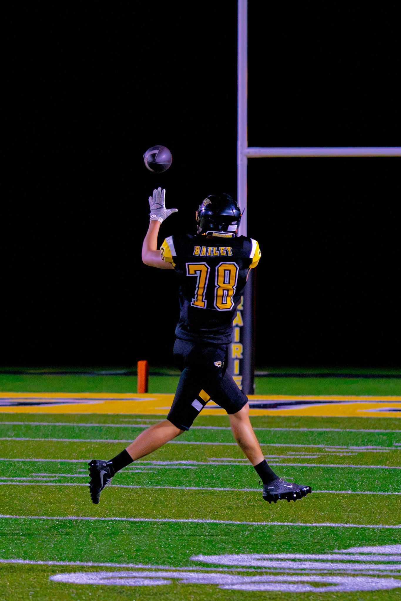 High school football player number 78 reaches up to catch a pass near the end zone during a night game.