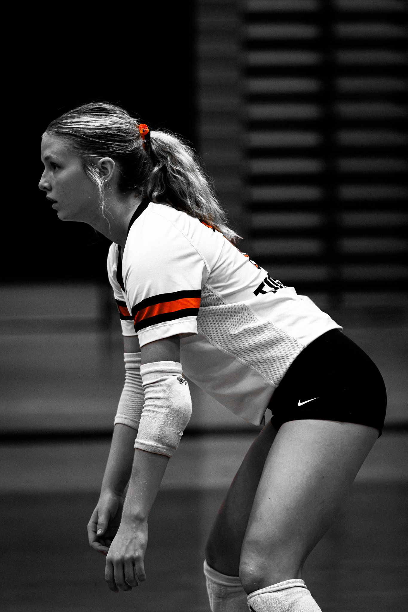Black and white photo of a female volleyball player in ready position wearing a white and orange jersey.