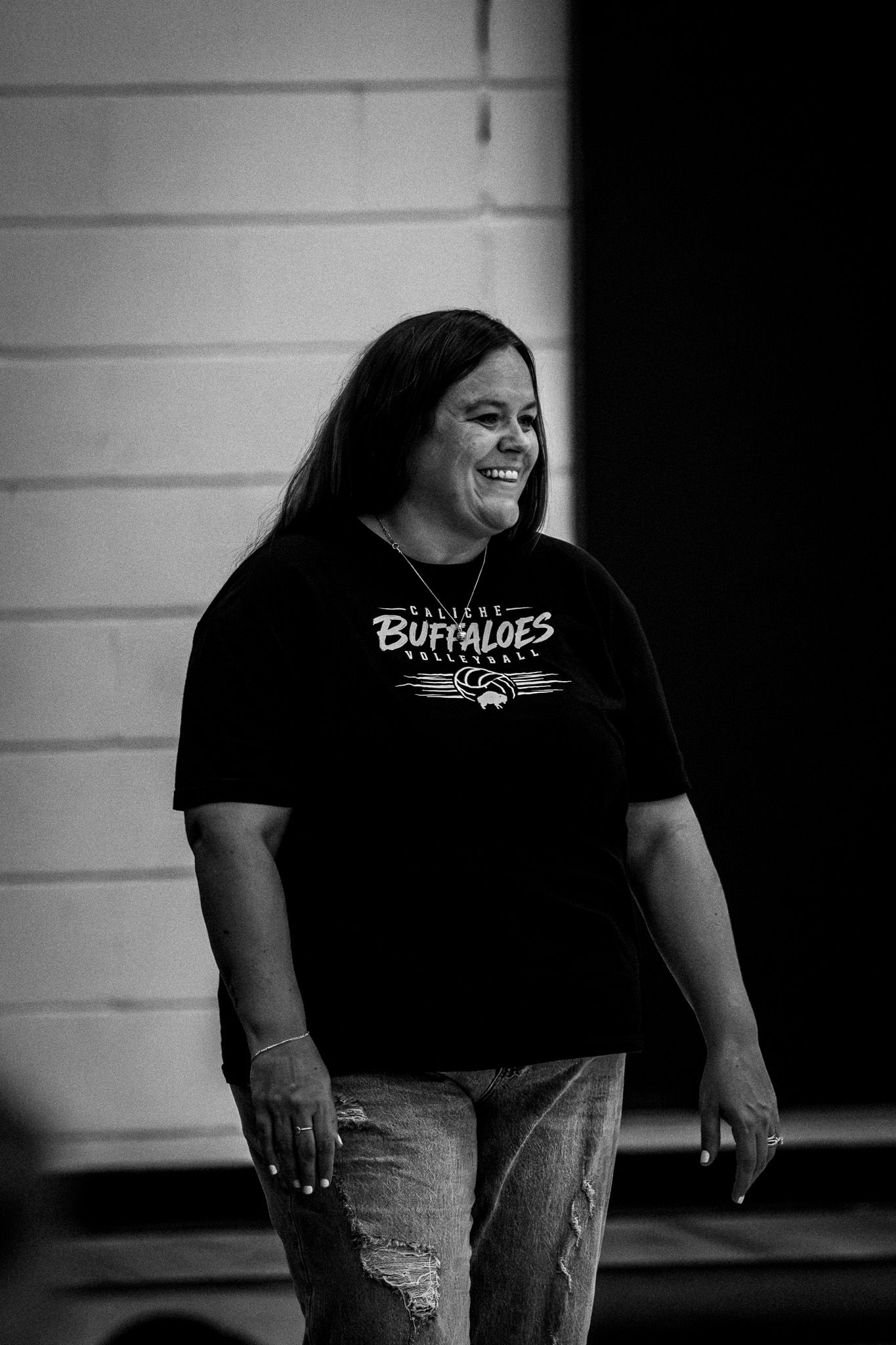 Smiling woman in black Buffaloes volleyball t-shirt and jeans in black and white photography.