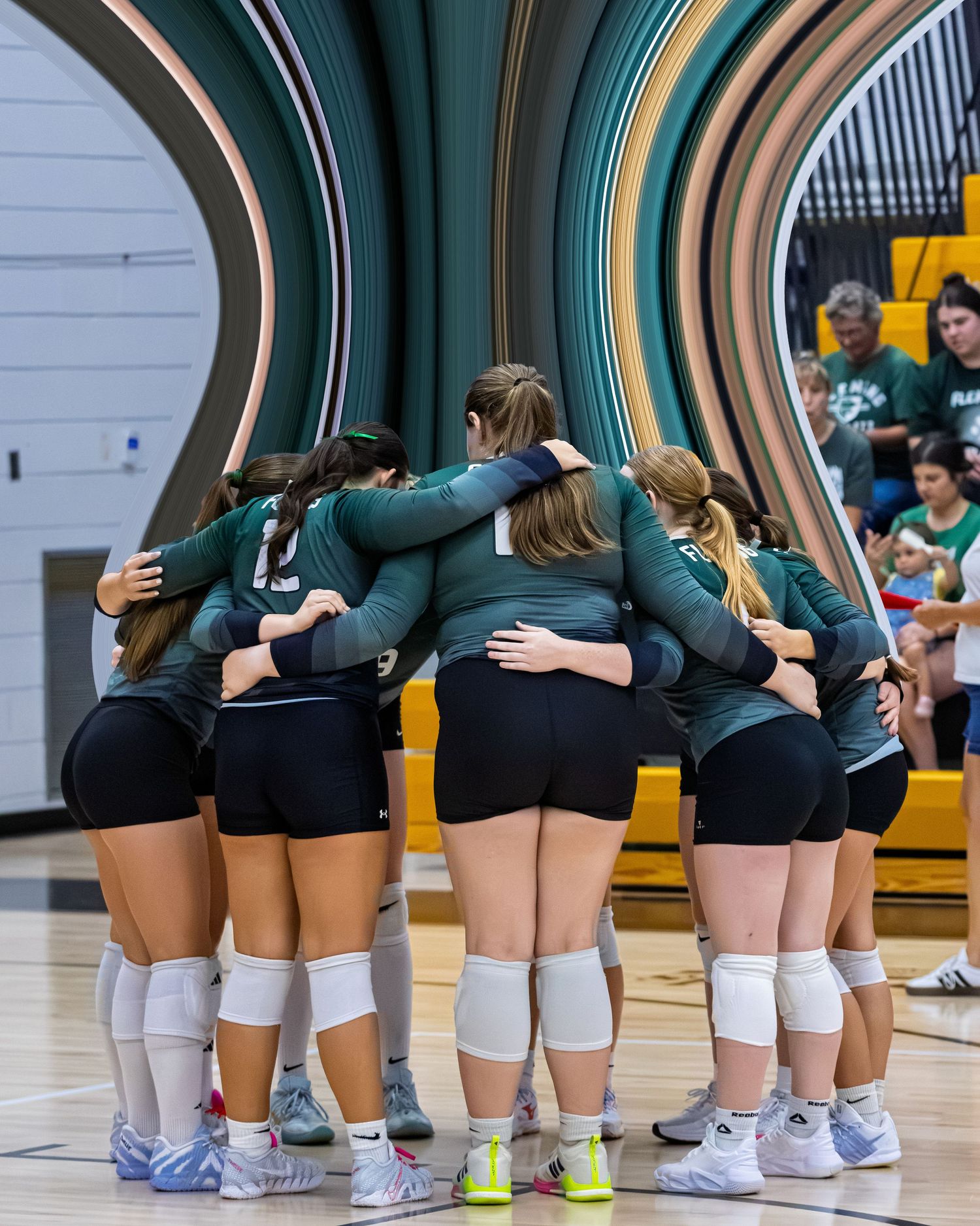 Girls volleyball team in green uniforms huddling together in circle on indoor court before match.