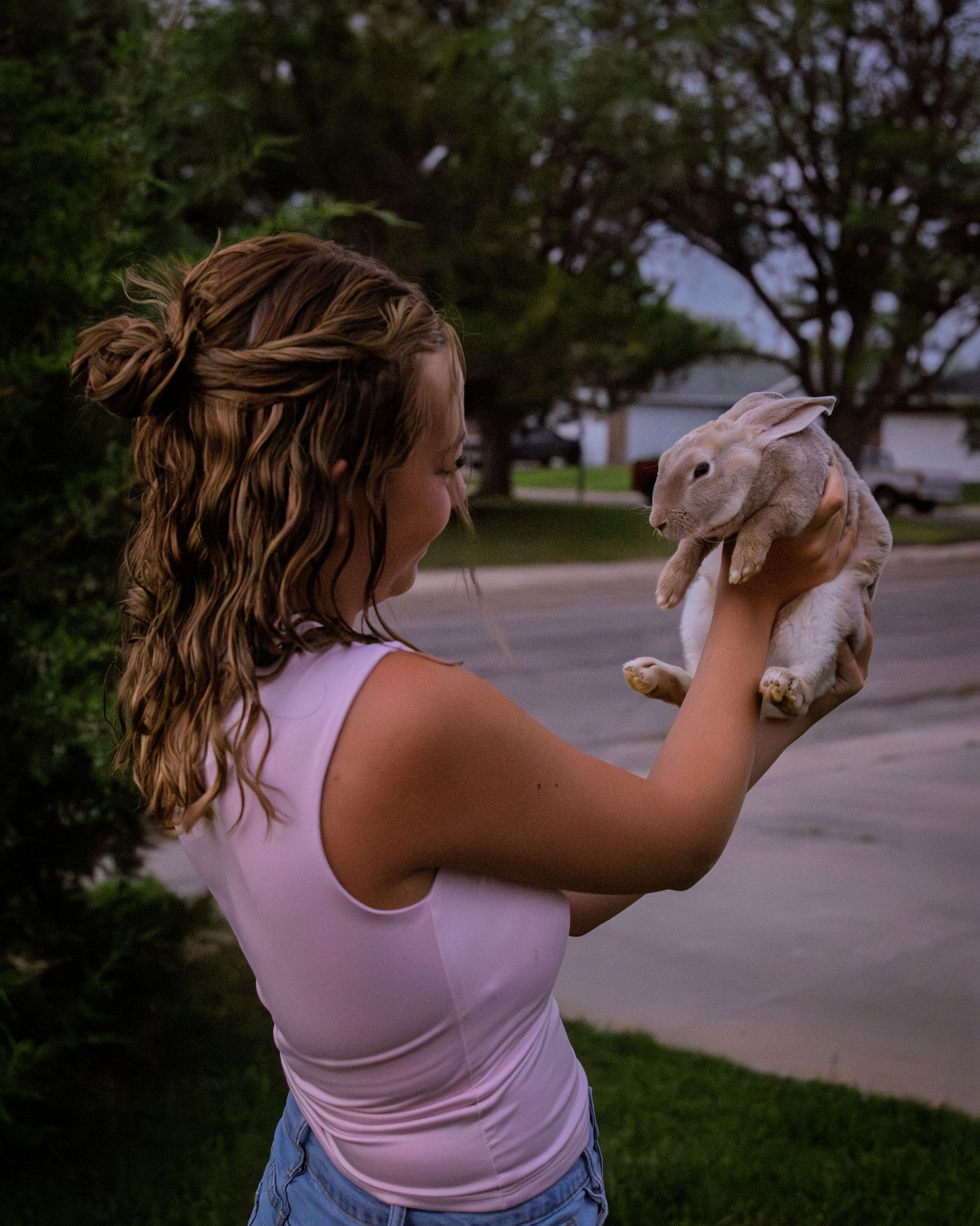 Girl with curly hair holding a rabbit up to examine it in a suburban backyard setting.