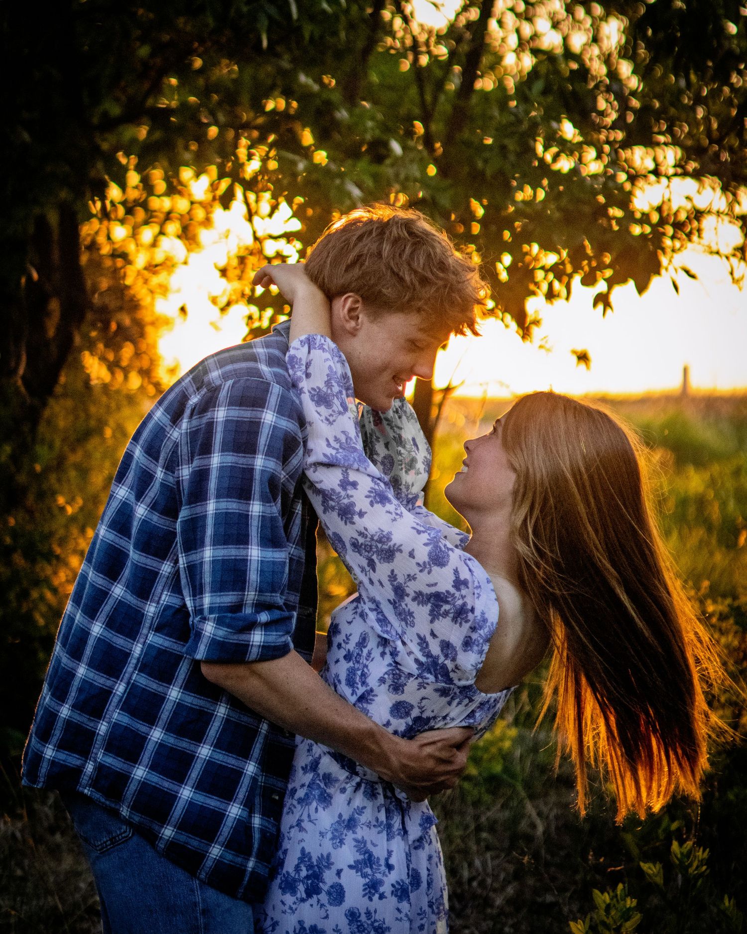 Young couple embracing tenderly in a sun-drenched field at golden hour with warm backlight.