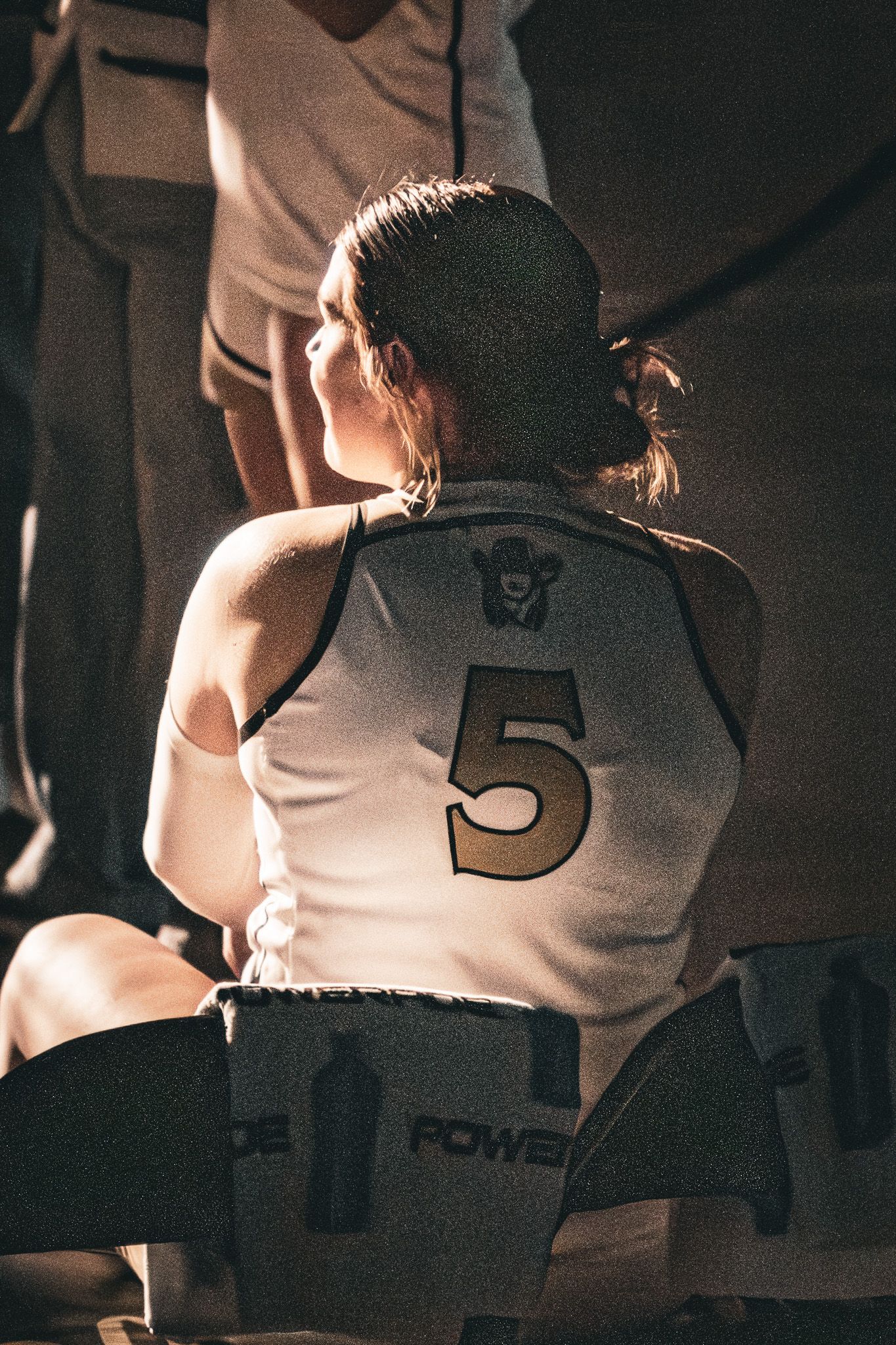 Female basketball player #5 sits on bench in white and gold Plainsmen jersey during a game.