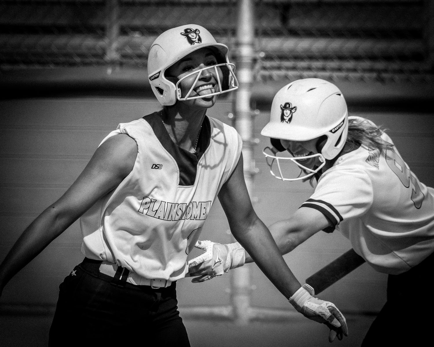 Two softball players celebrate in black and white photo during outdoor game.