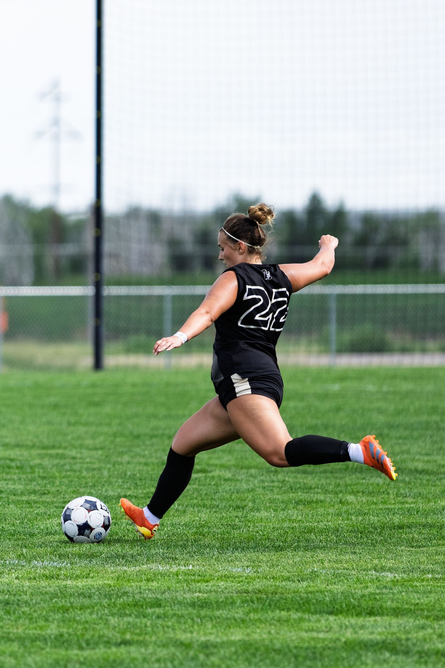 Female soccer player number 22 in black uniform preparing to kick ball on green turf field.