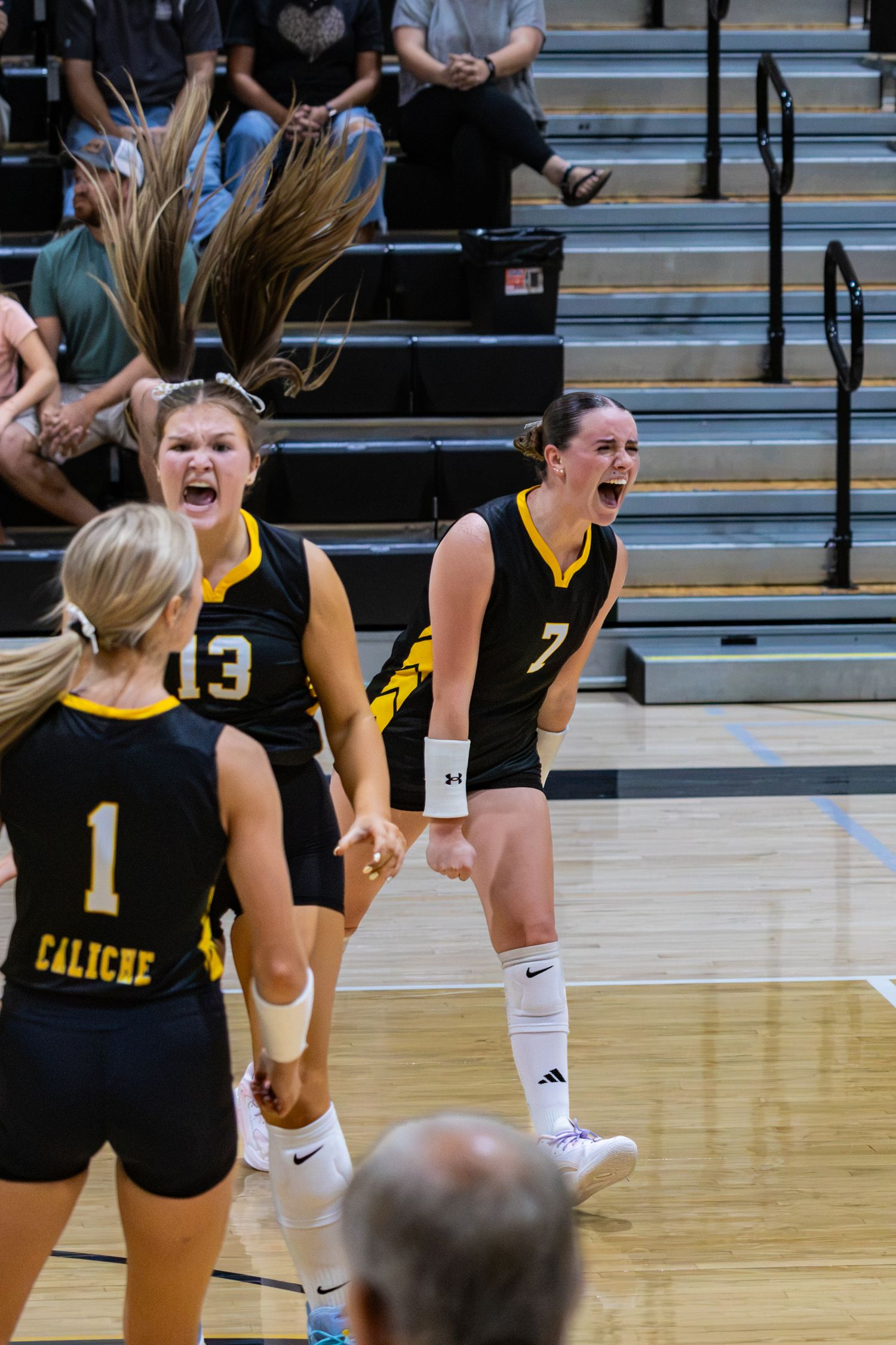 Caliche volleyball players in black and gold uniforms celebrate a point during a competitive match.