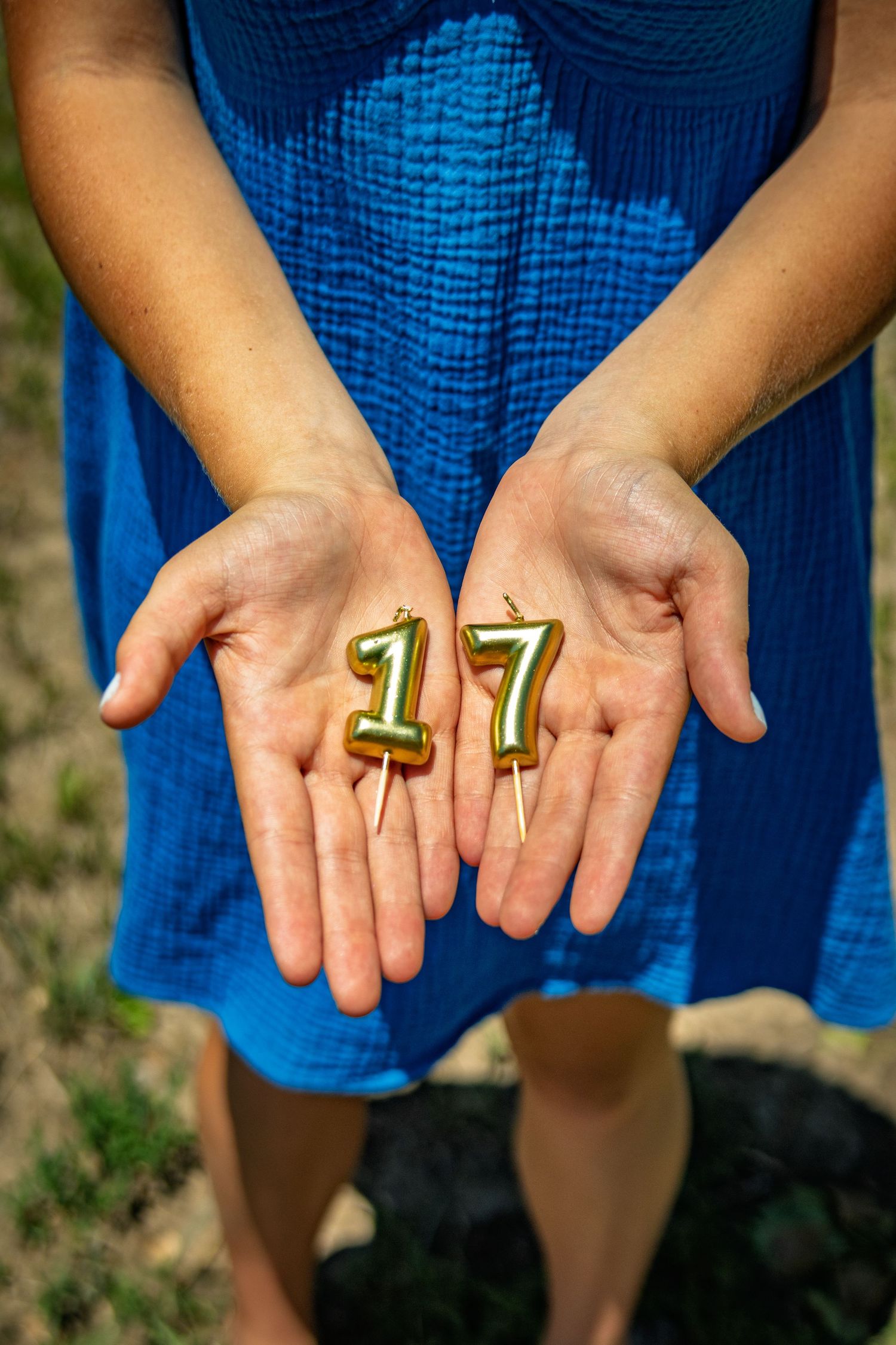 Hands holding gold number 17 birthday candles outdoors in natural light.