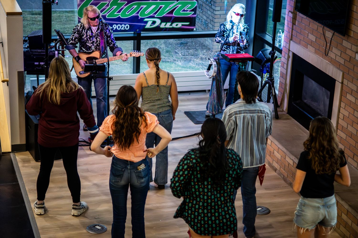 Audience members dance in front of live band performing at indoor venue with neon green signage.