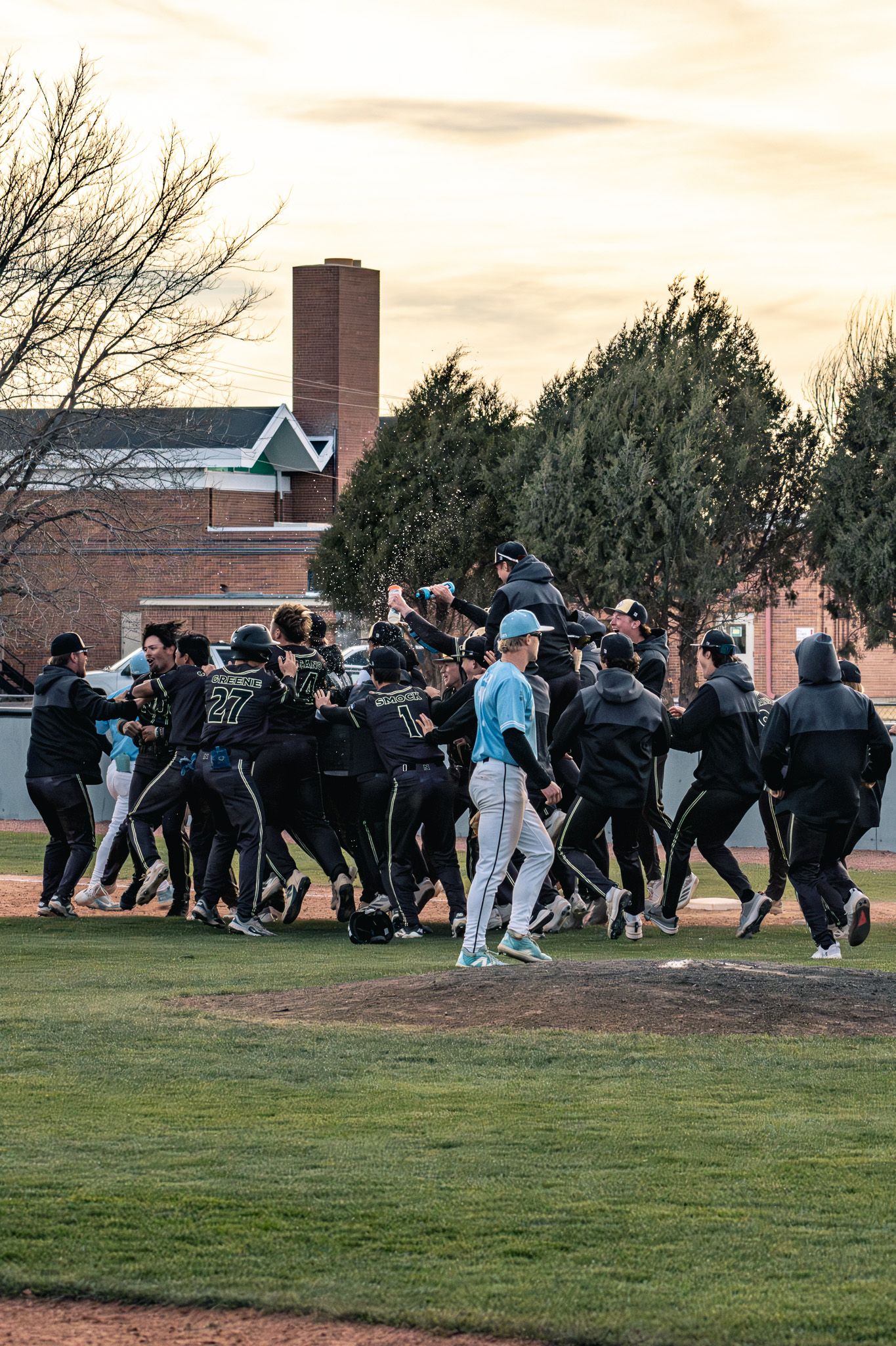 Baseball team celebrates victory in dogpile on field at sunset.