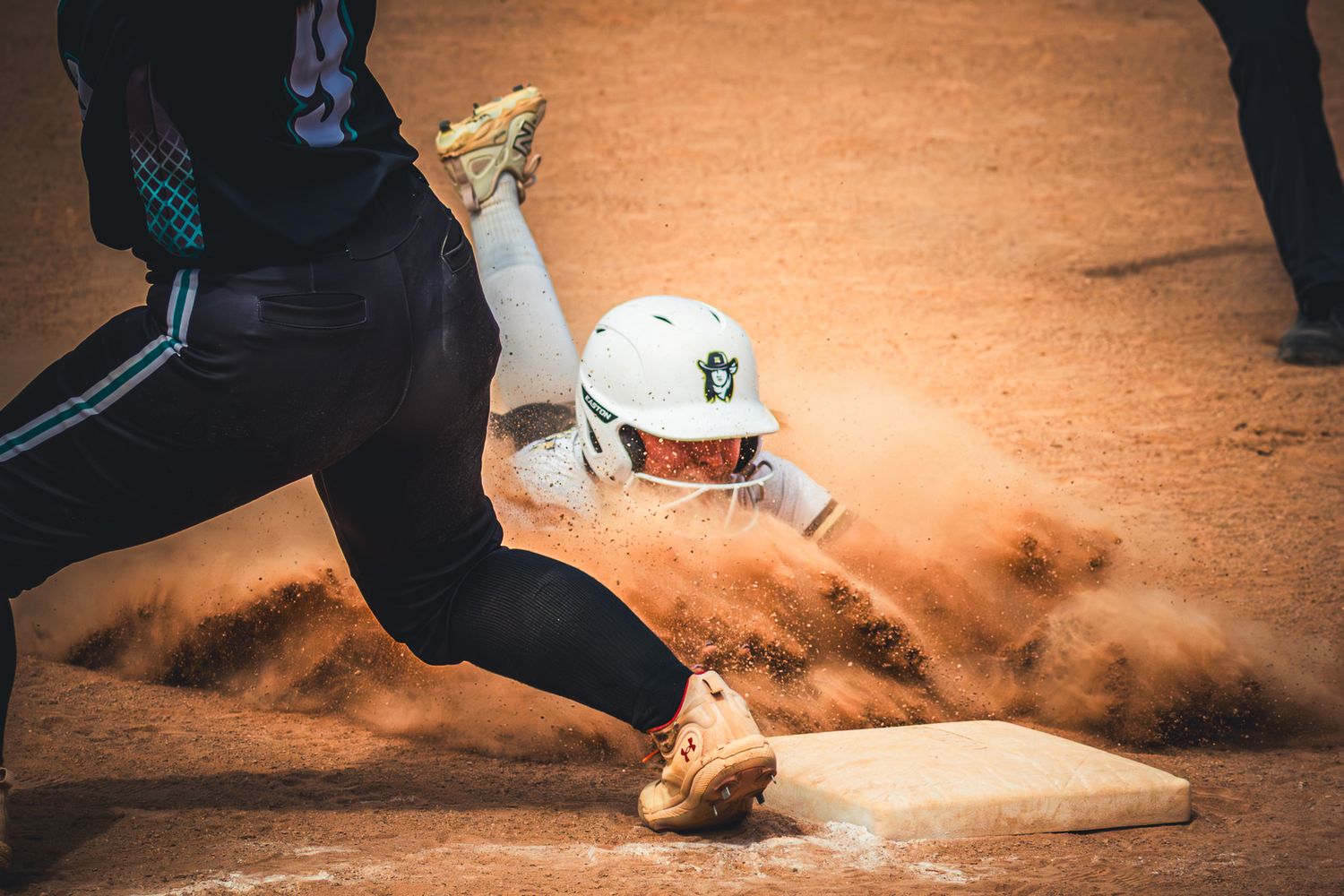 Softball player slides into base creating dramatic dust cloud during competitive game.