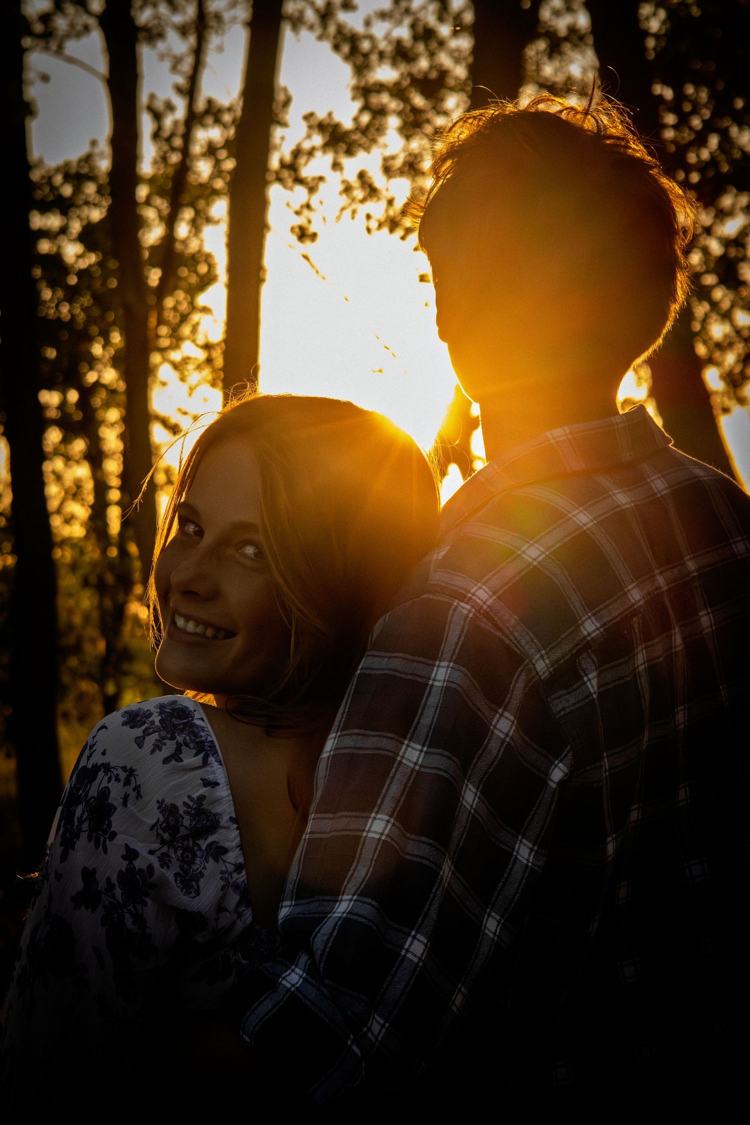 Romantic couple silhouetted against a warm golden sunset light filtering through forest trees.