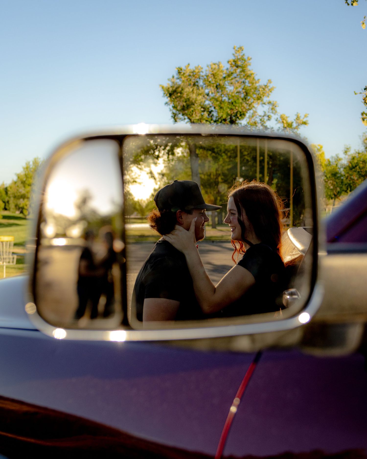 Romantic couple reflected in a vintage truck side mirror during golden hour at sunset.