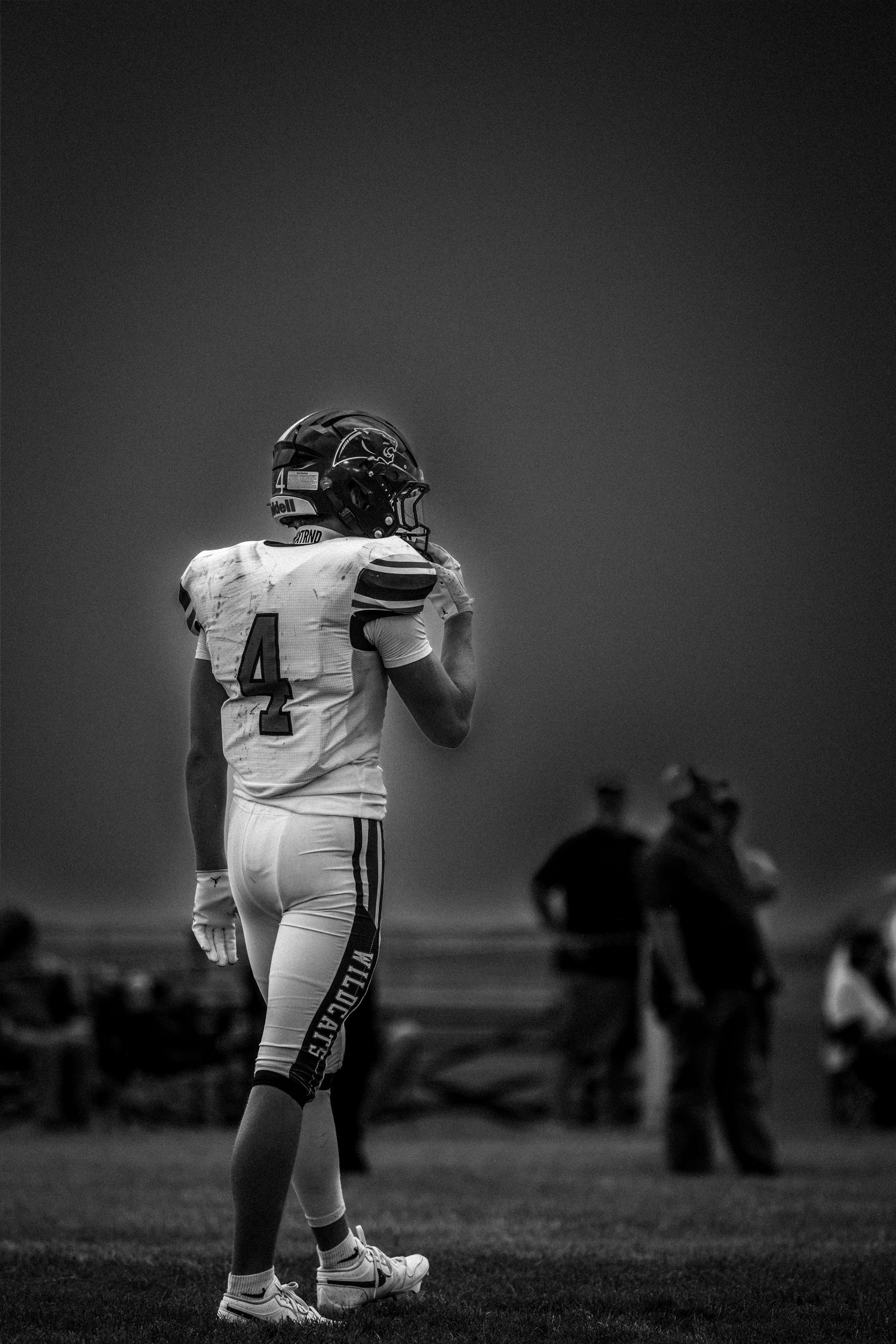 A Wildcats number 4 football player stands alone in black and white on the sideline.